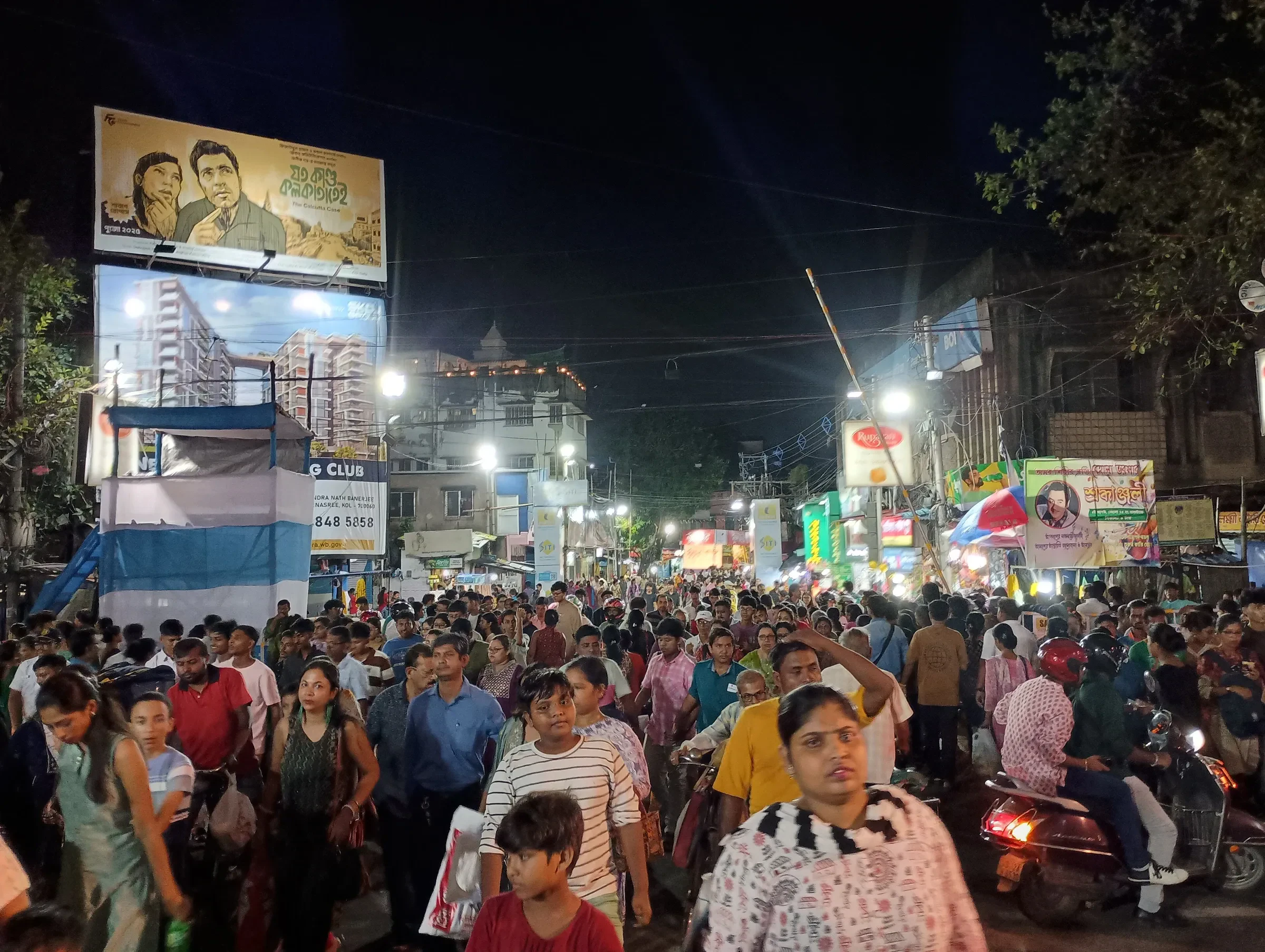 A dense crowd filling a street at night in Behala, Kolkata, during Durga Puja