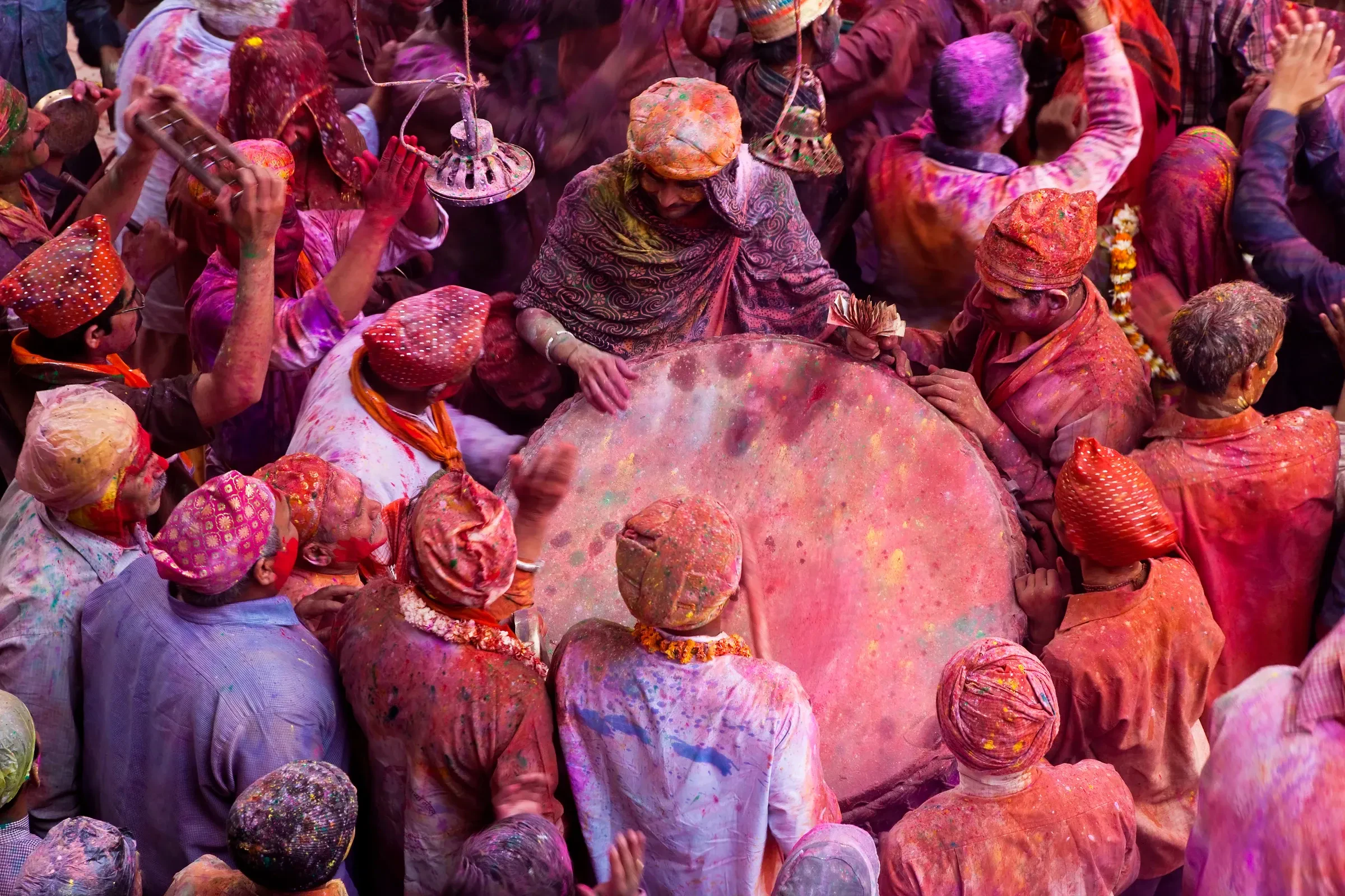 Crowds covered in pink and purple colour at a Holi celebration in a temple courtyard