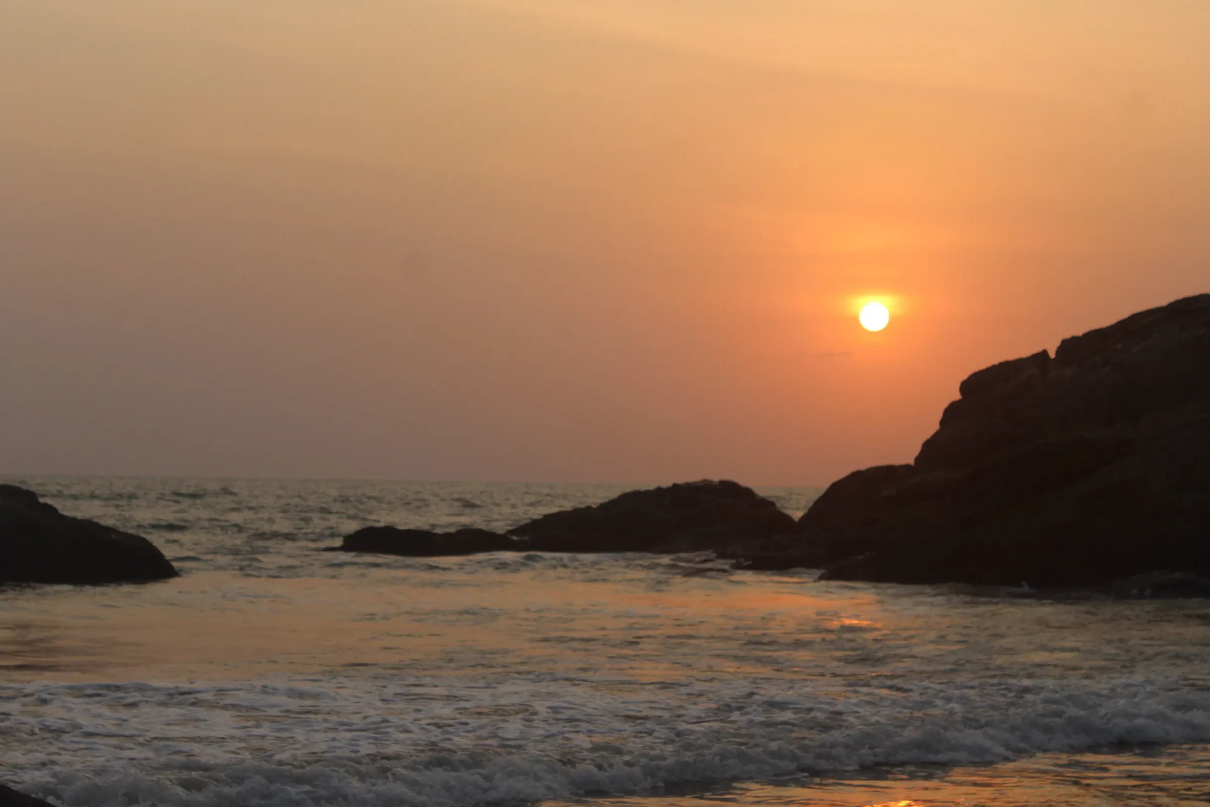 Sunset over the sea and dark rocks at Kudle Beach, Gokarna