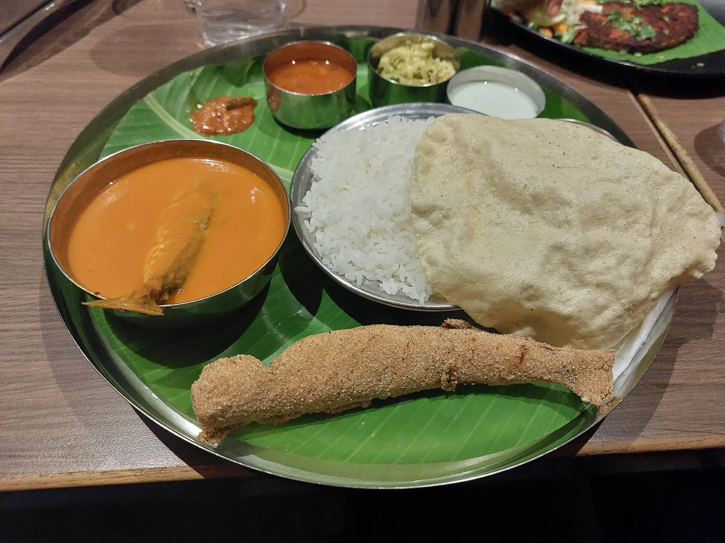 A Mangalore fish curry meal with rice and papad on a steel plate