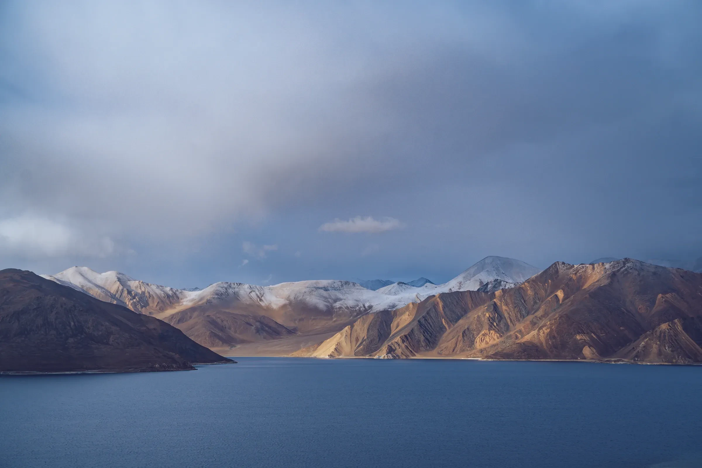 Pangong Lake in Ladakh under a cloudy sky with snow-dusted mountains beyond