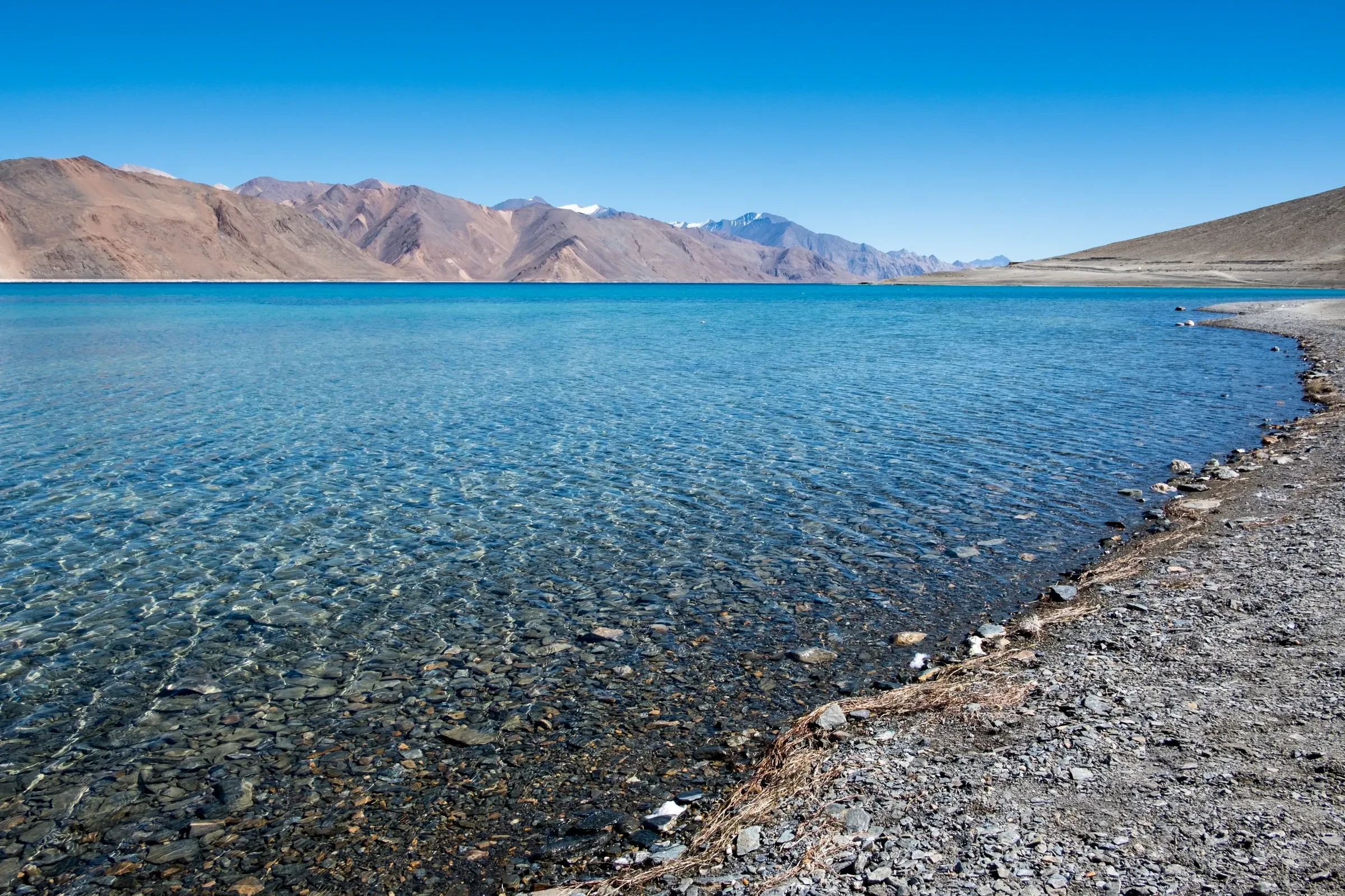 The clear blue water of Pangong Lake with brown mountains behind