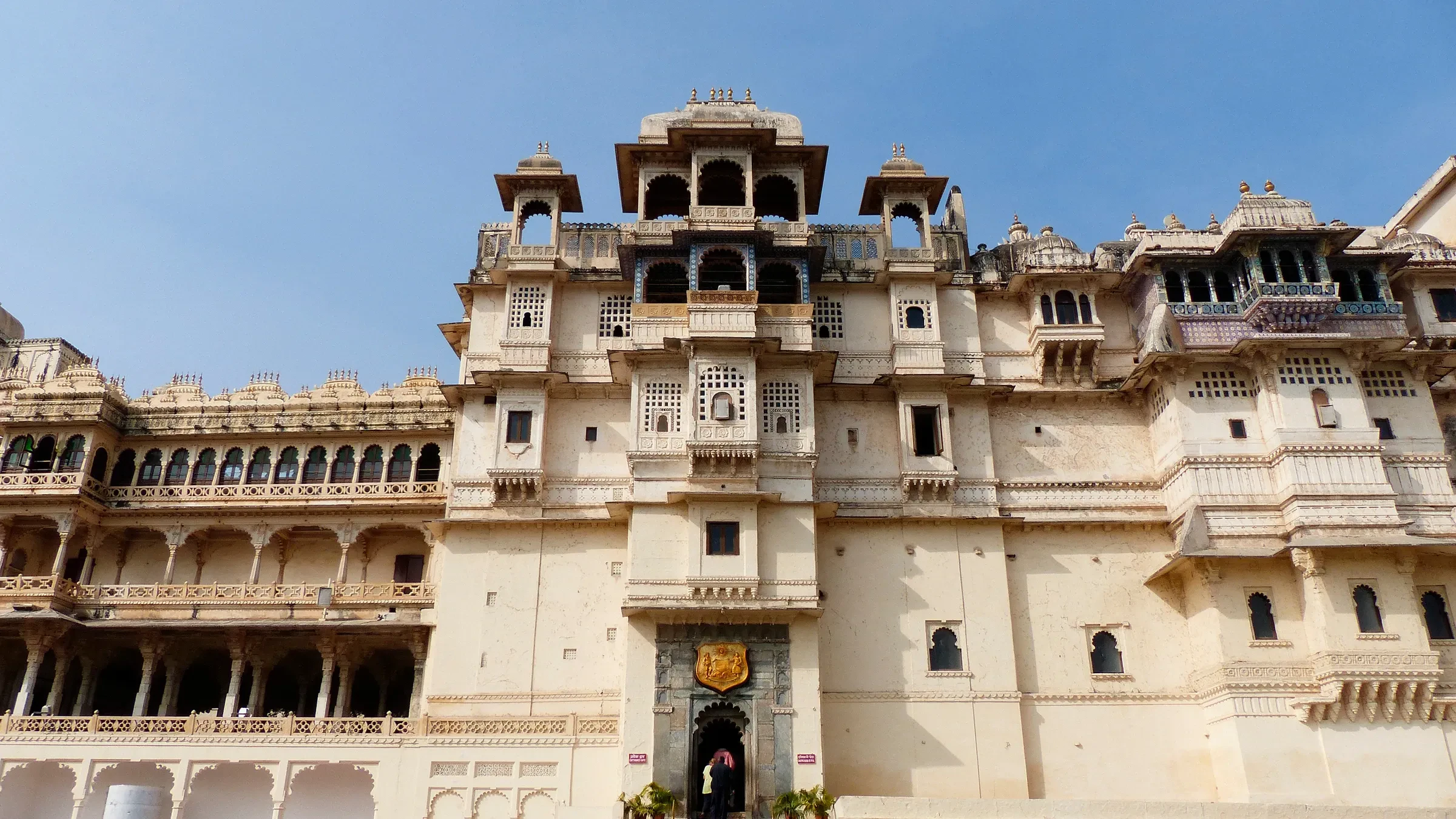 The City Palace of Udaipur rising above the old city, seen from below against a blue sky