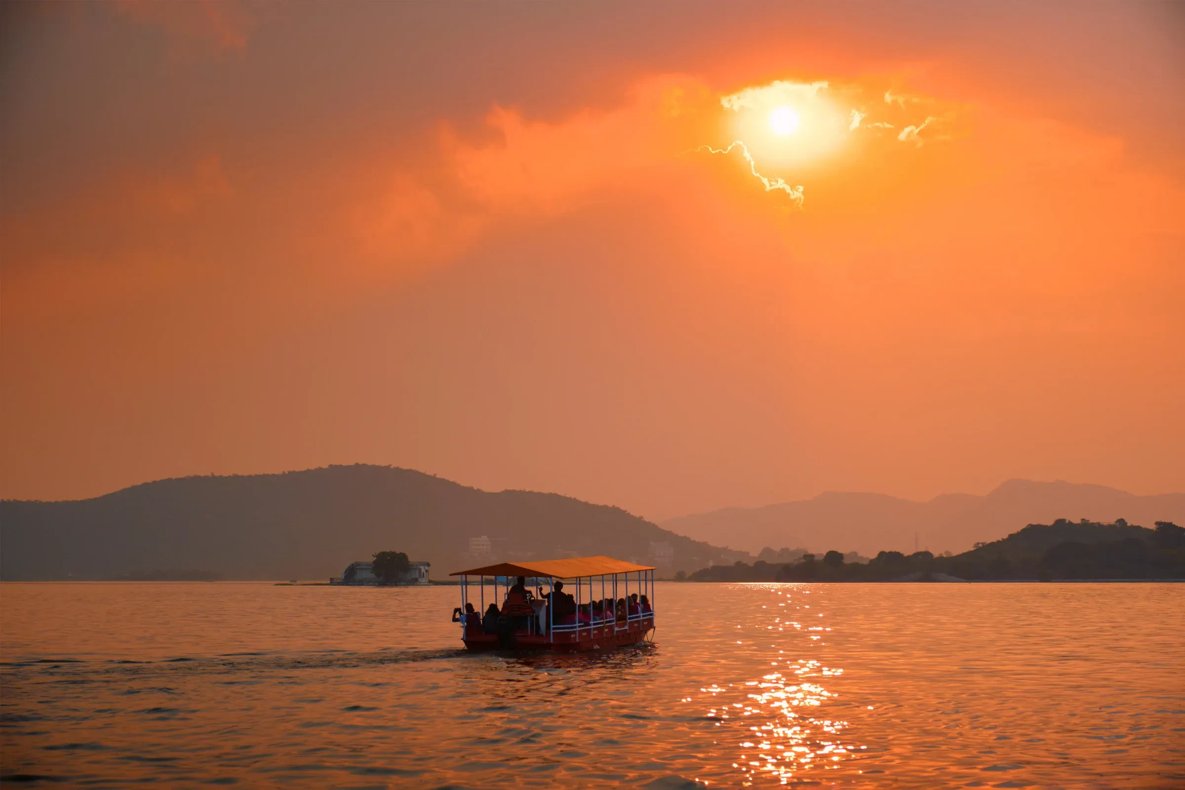 A covered boat on Lake Pichola under an orange sunset sky