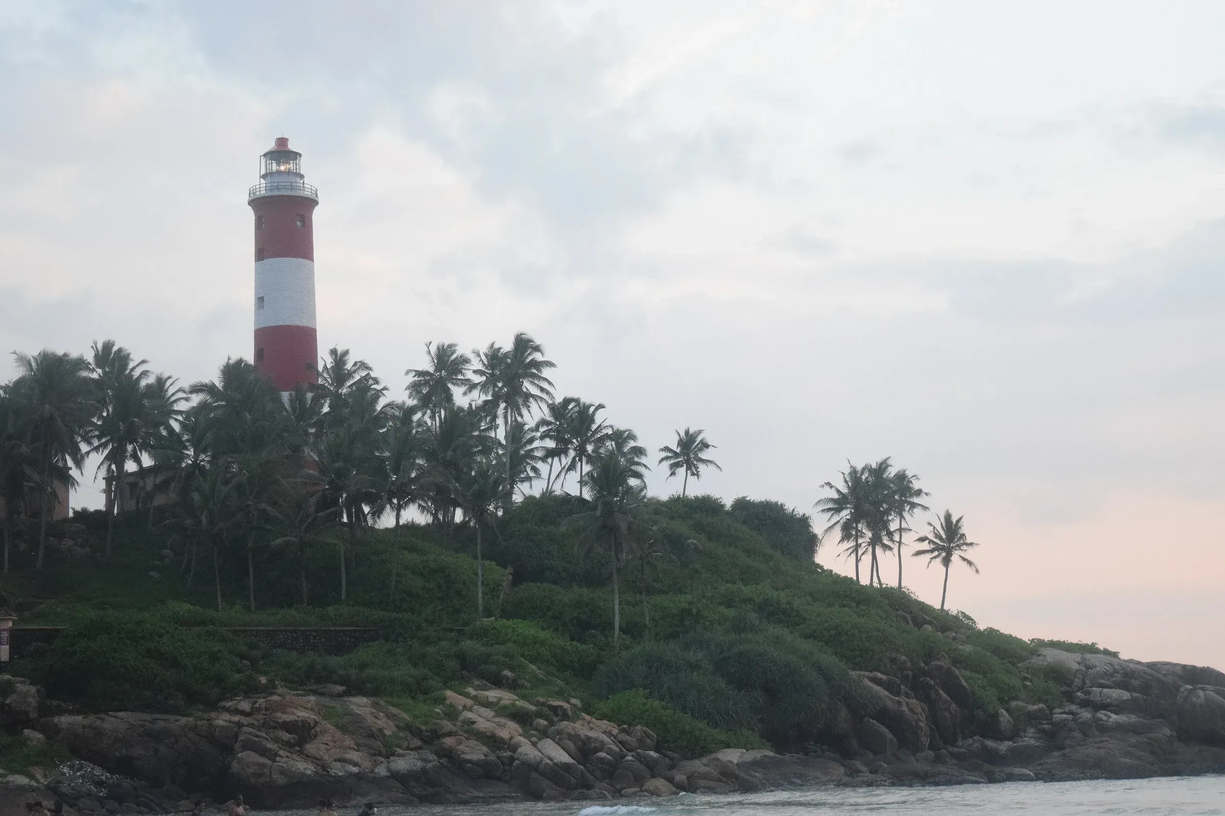Lighthouse Beach at Kovalam with the red and white lighthouse above the palms and rocks