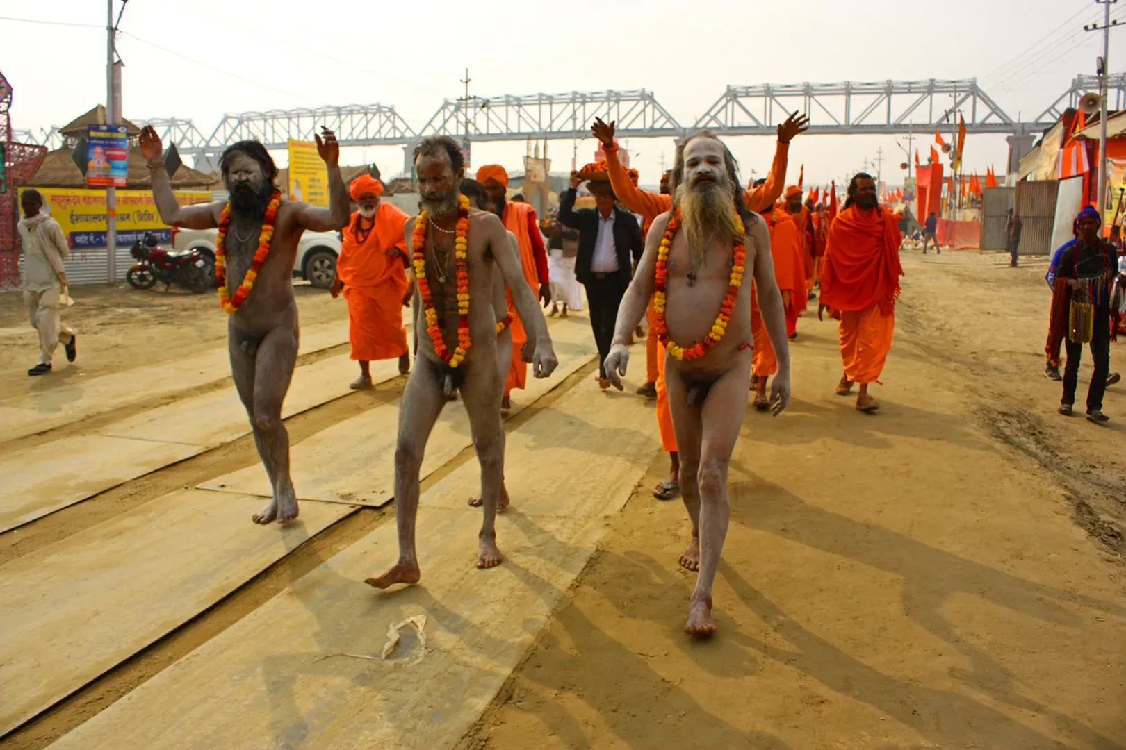 Naga sadhus, ash-smeared ascetics, walking in a procession along a dirt road at a Kumbh Mela