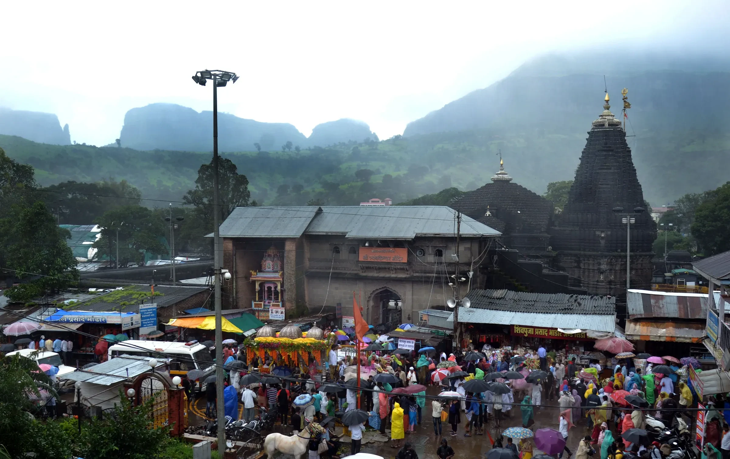 Trimbakeshwar Shiva Temple with green hills behind it and a crowd of pilgrims in the foreground