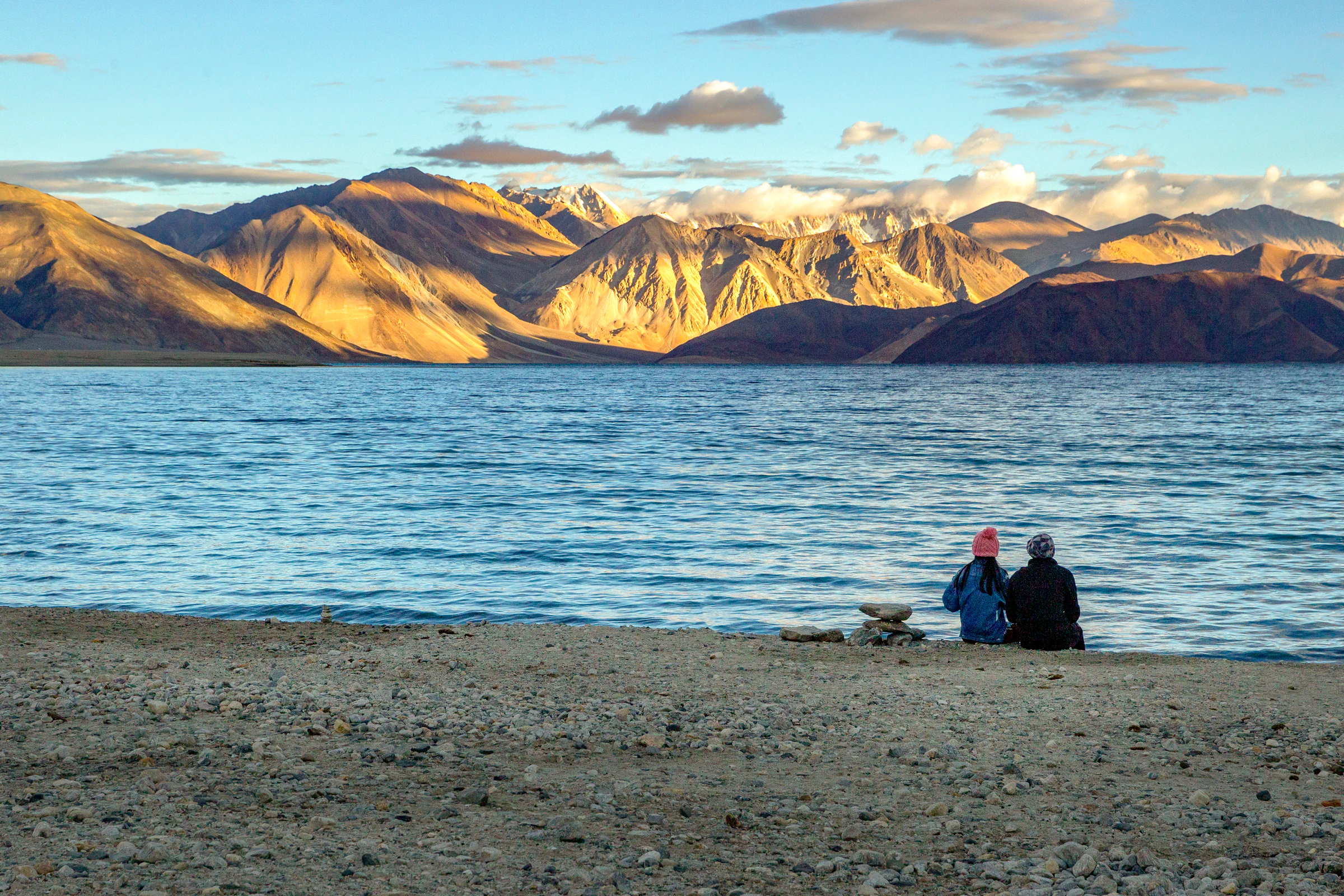 A couple watching sunrise over Pangong Lake's turquoise water in Ladakh