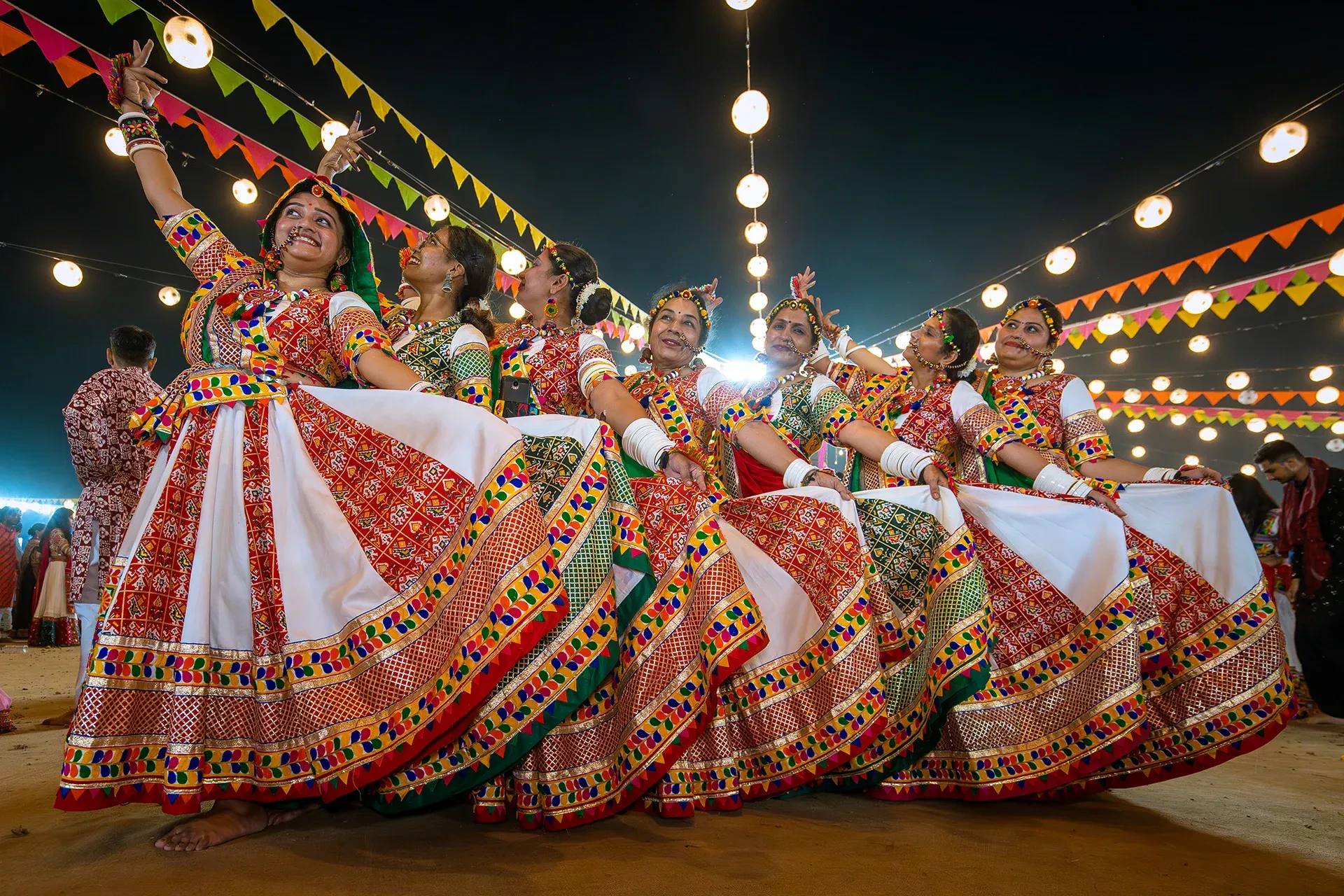 Dancers in traditional dress performing Garba under string lights at a Navratri celebration