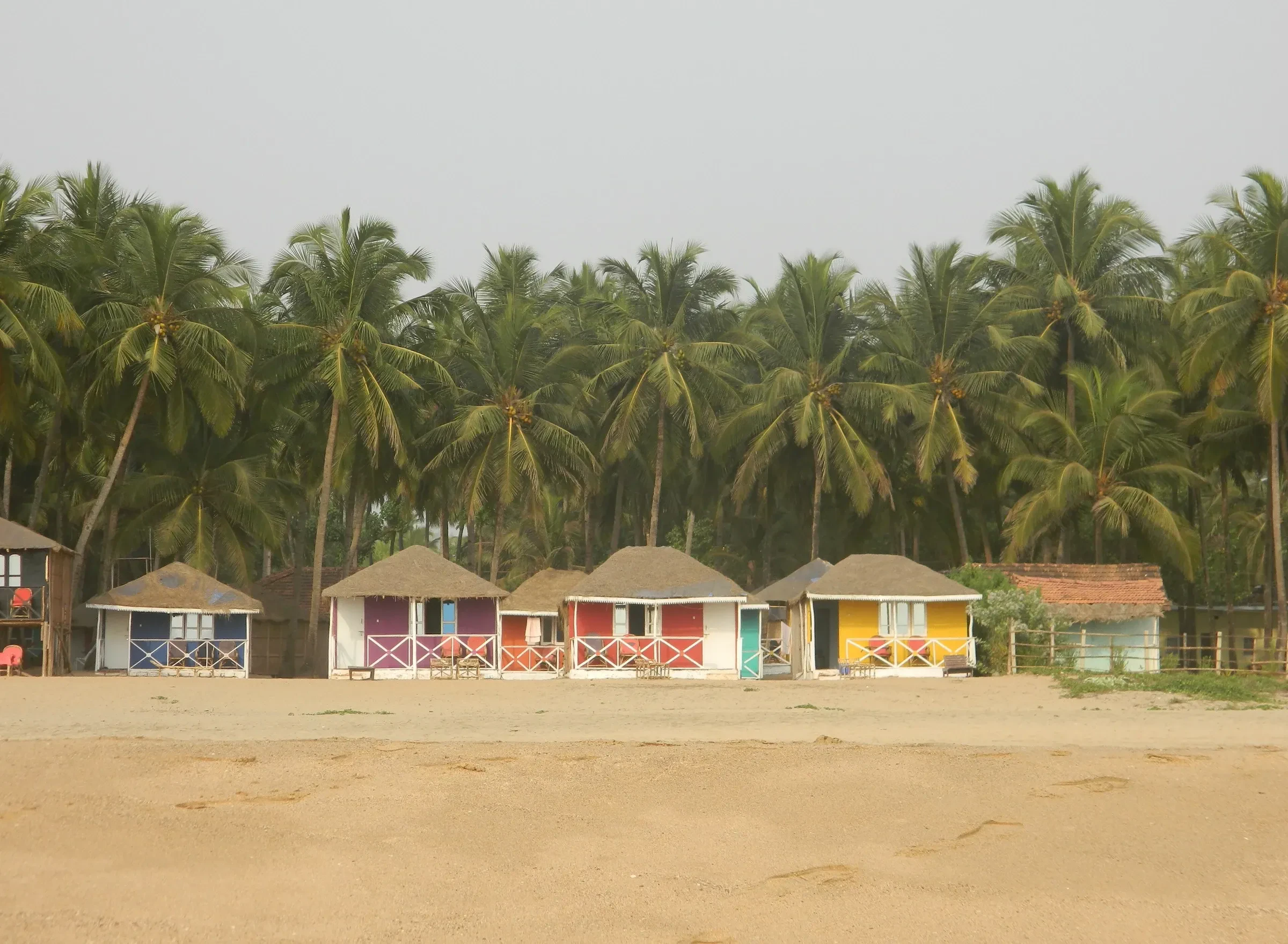 Pastel beach huts under palm trees at Agonda beach in South Goa