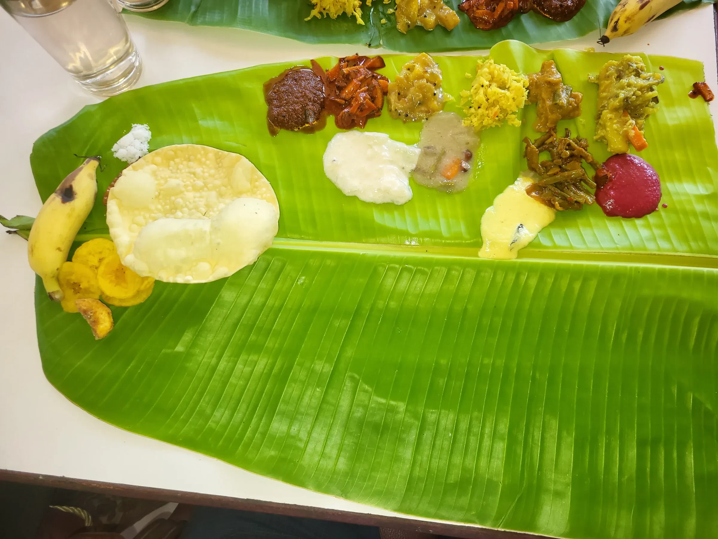 An Onam sadya on a banana leaf, with small portions of curries, pickles and a papadam