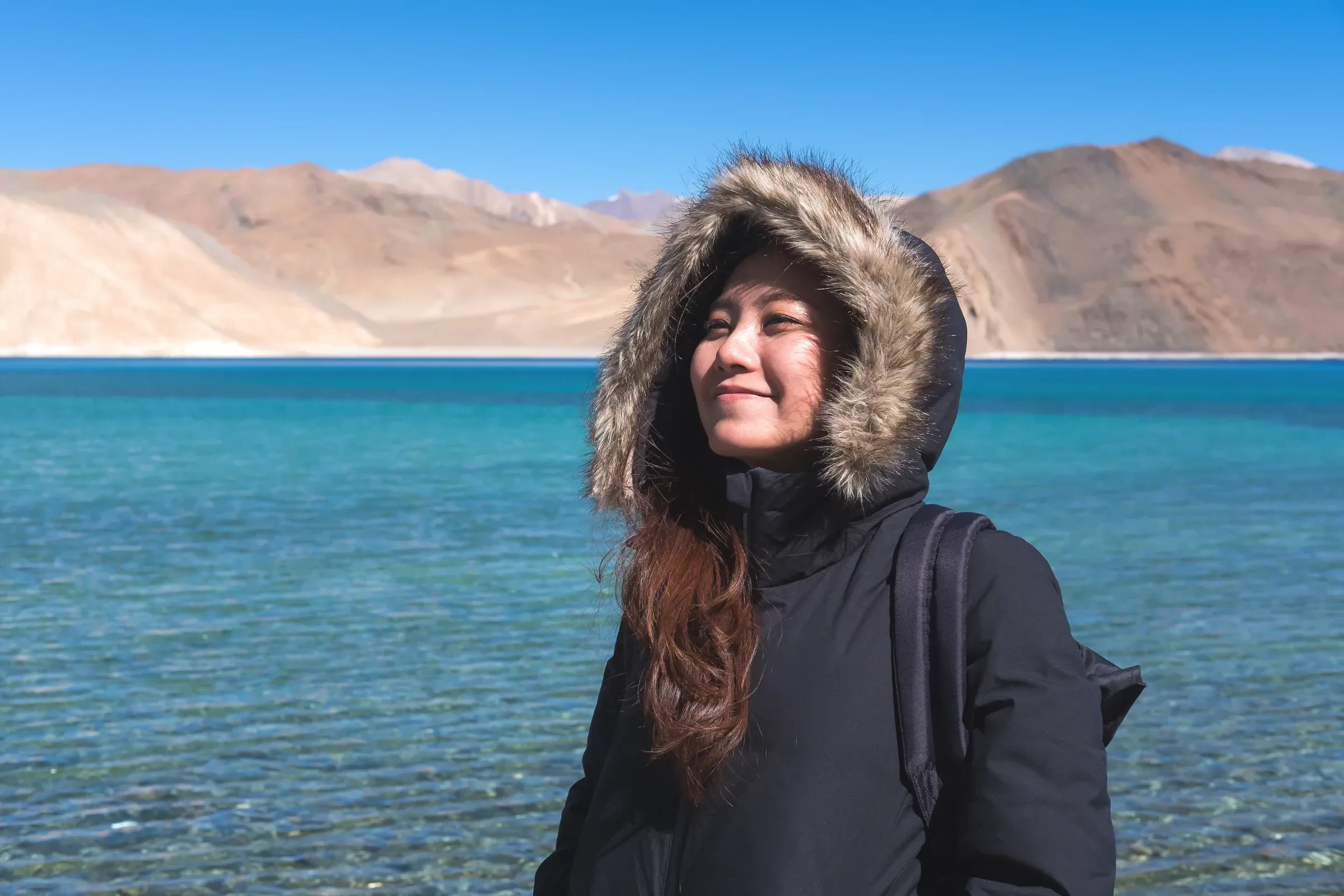 A traveller in a fur-trimmed hooded jacket beside Pangong Lake in Ladakh