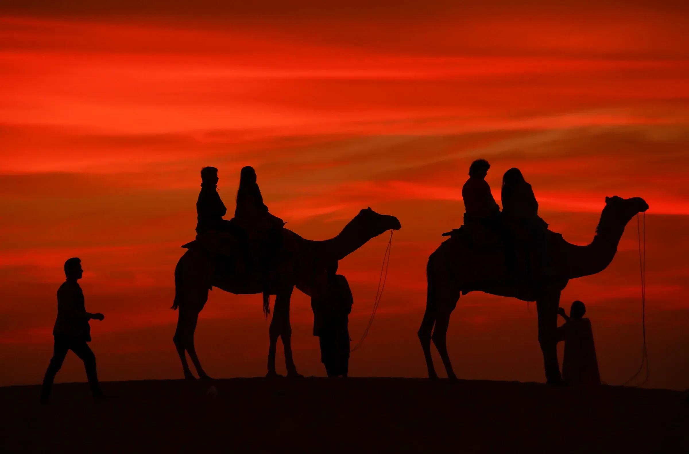 Two riders on camels in silhouette against a red evening sky at Sam Sand Dunes near Jaisalmer