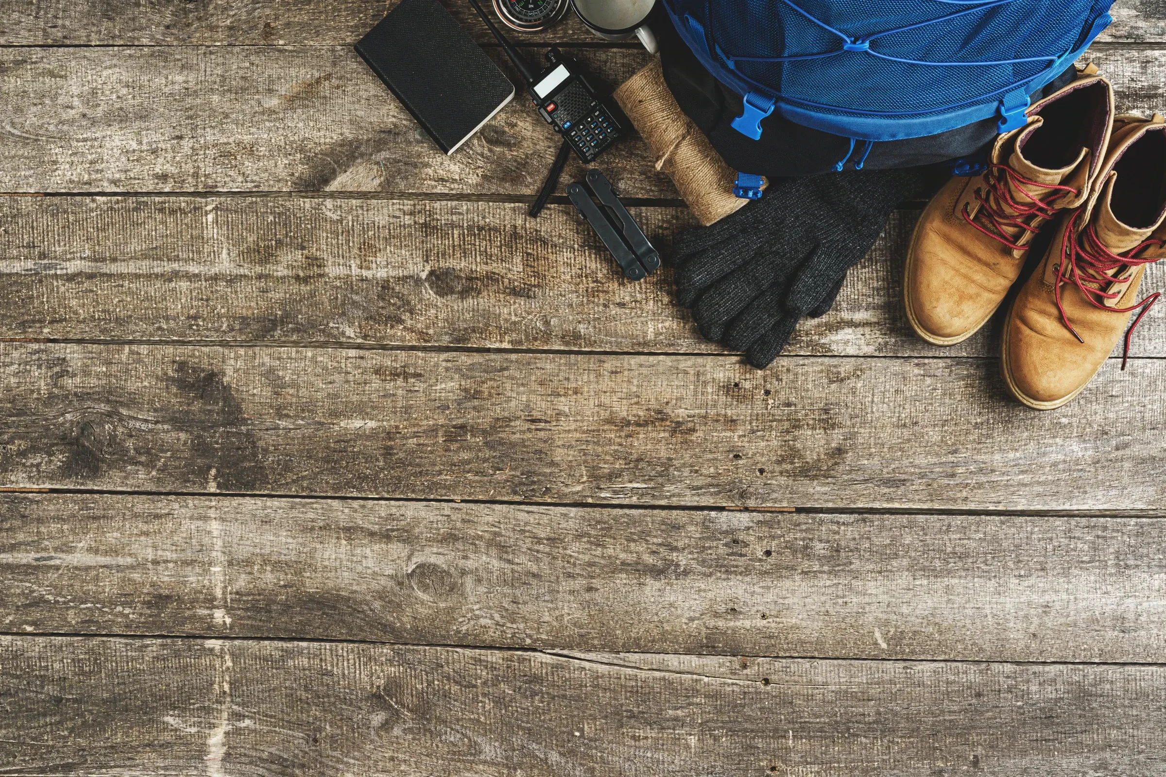 Hiking boots, a backpack, gloves and a notebook laid out on weathered wooden boards