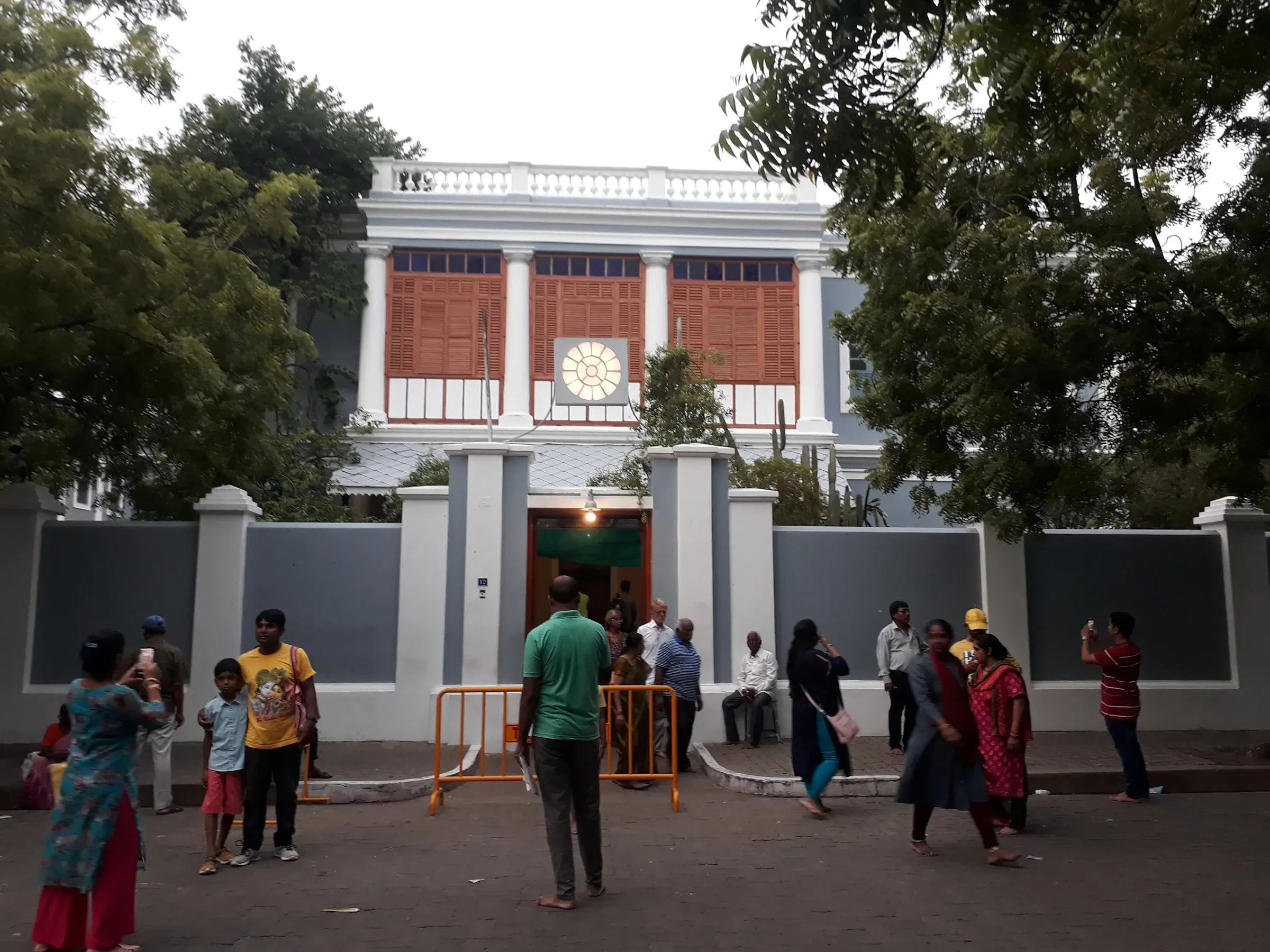 The Sri Aurobindo Ashram's pale facade and entrance gate in Pondicherry, with visitors outside