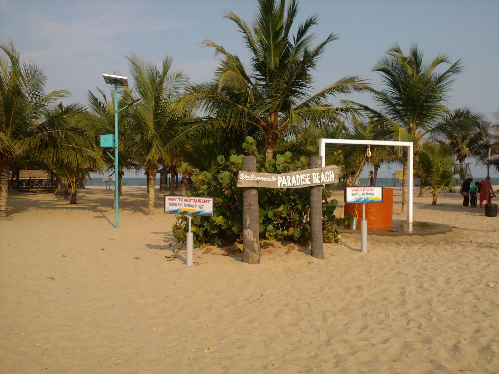 A sandy beach with palm trees and a Paradise Beach sign near Chunnambar, Pondicherry