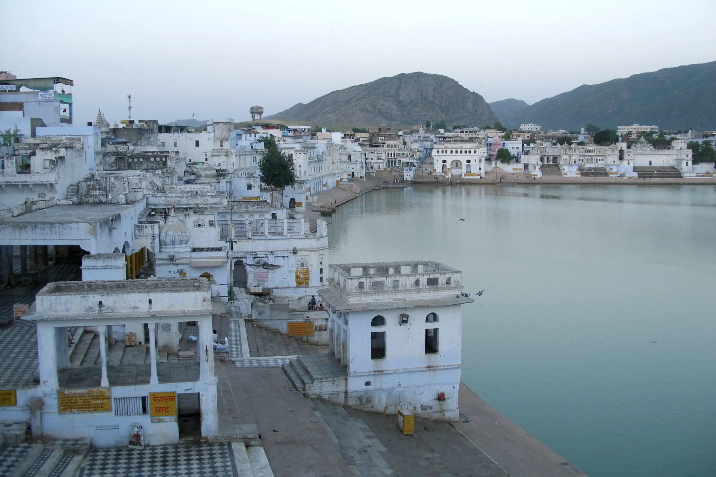 Pushkar Lake and the white ghats at twilight, with hills behind the town