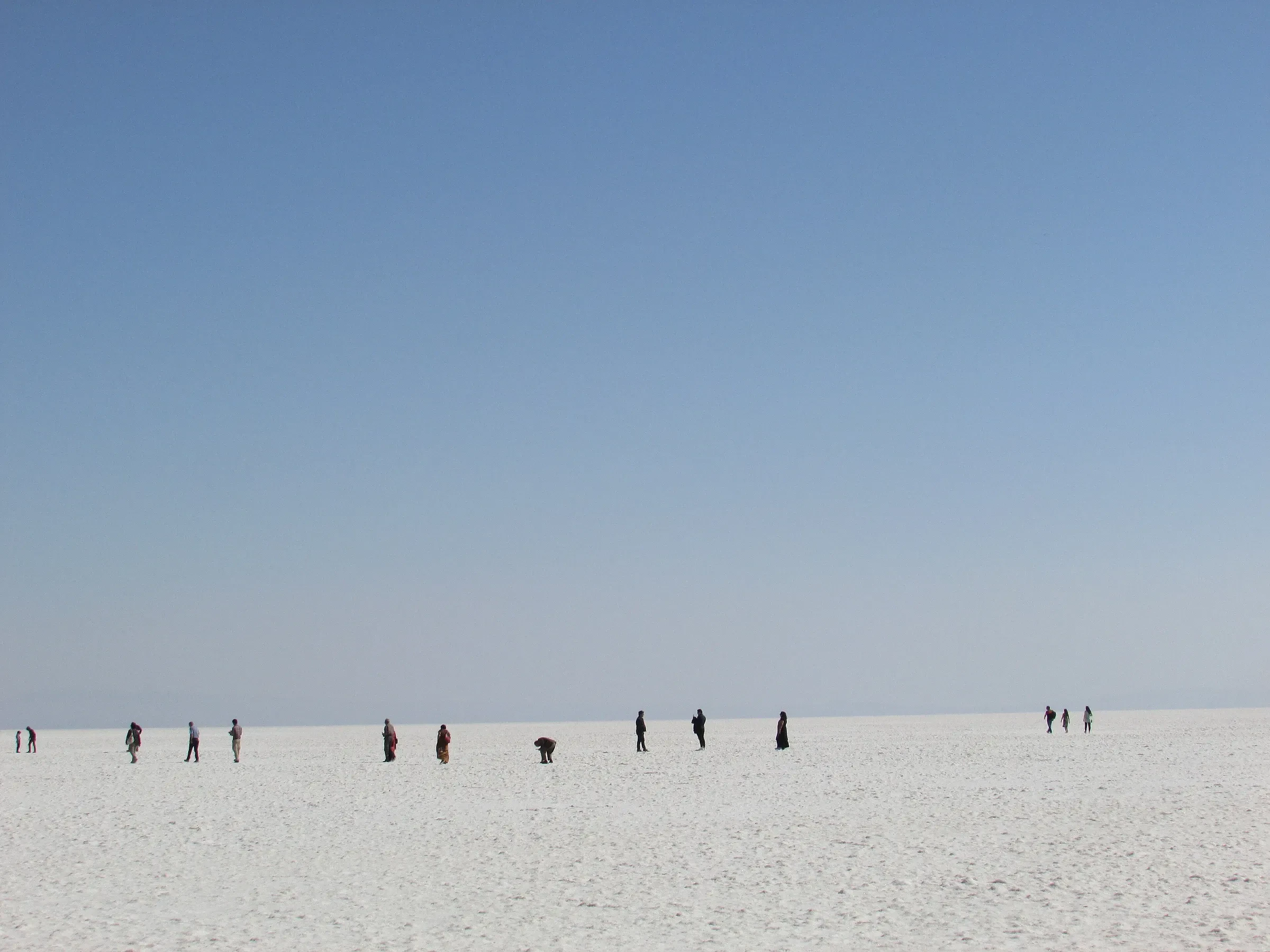 People walking across the white salt crust of the Great Rann of Kutch under a clear blue sky