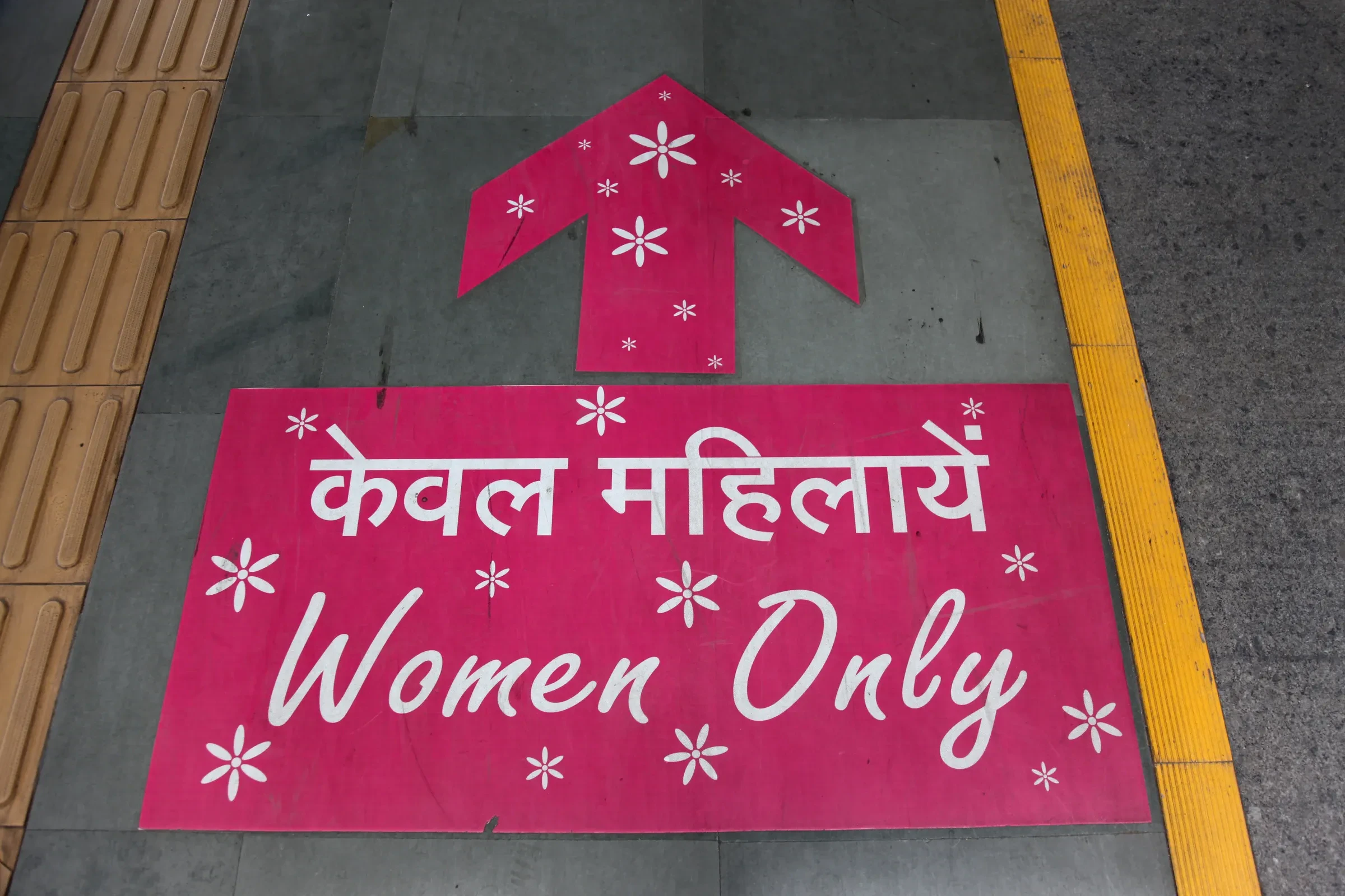 A pink floor sign reading Women Only in Hindi and English, marking where the women's coach stops on a Delhi Metro platform