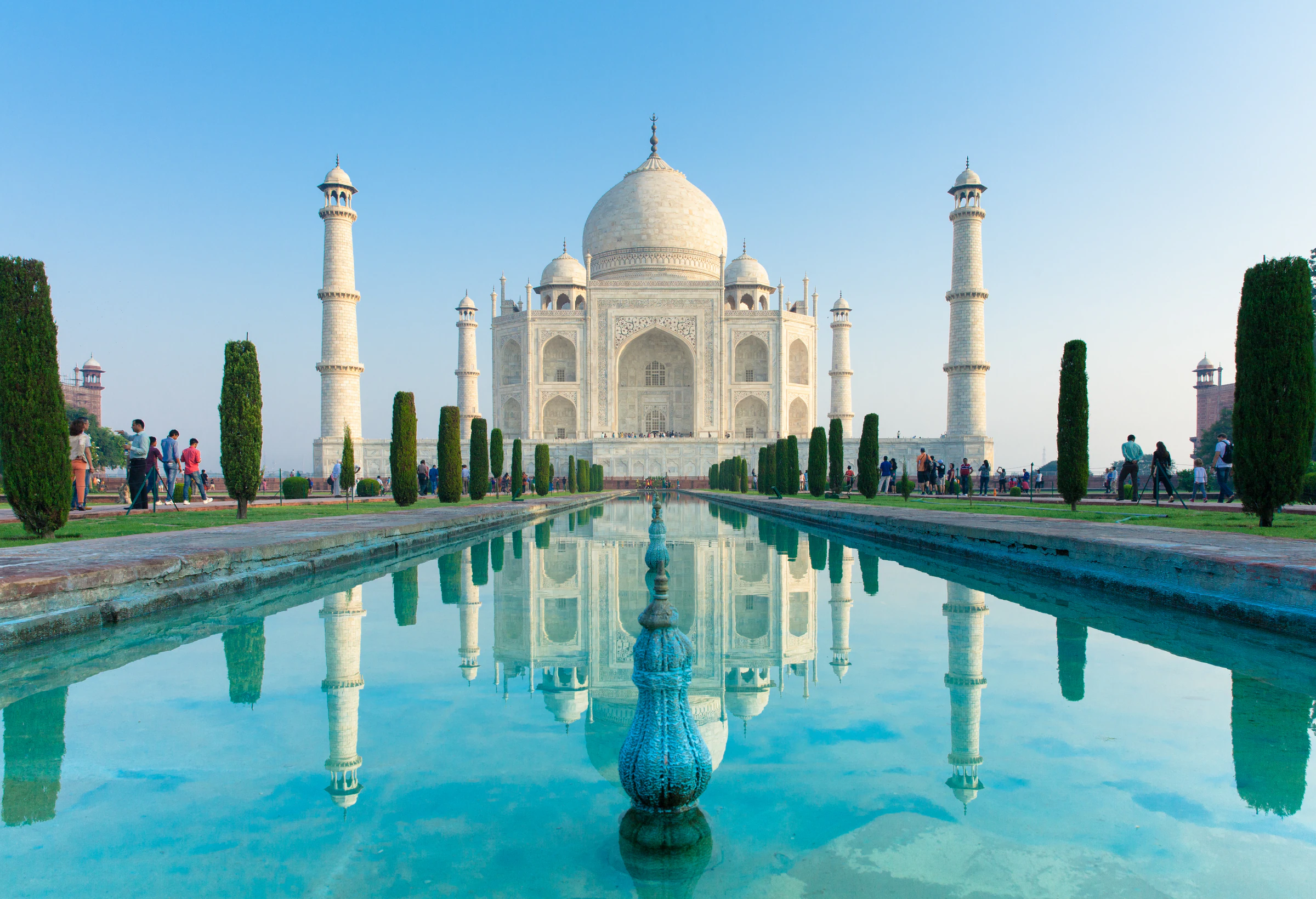 The Taj Mahal reflected in its long garden pool under a clear sky