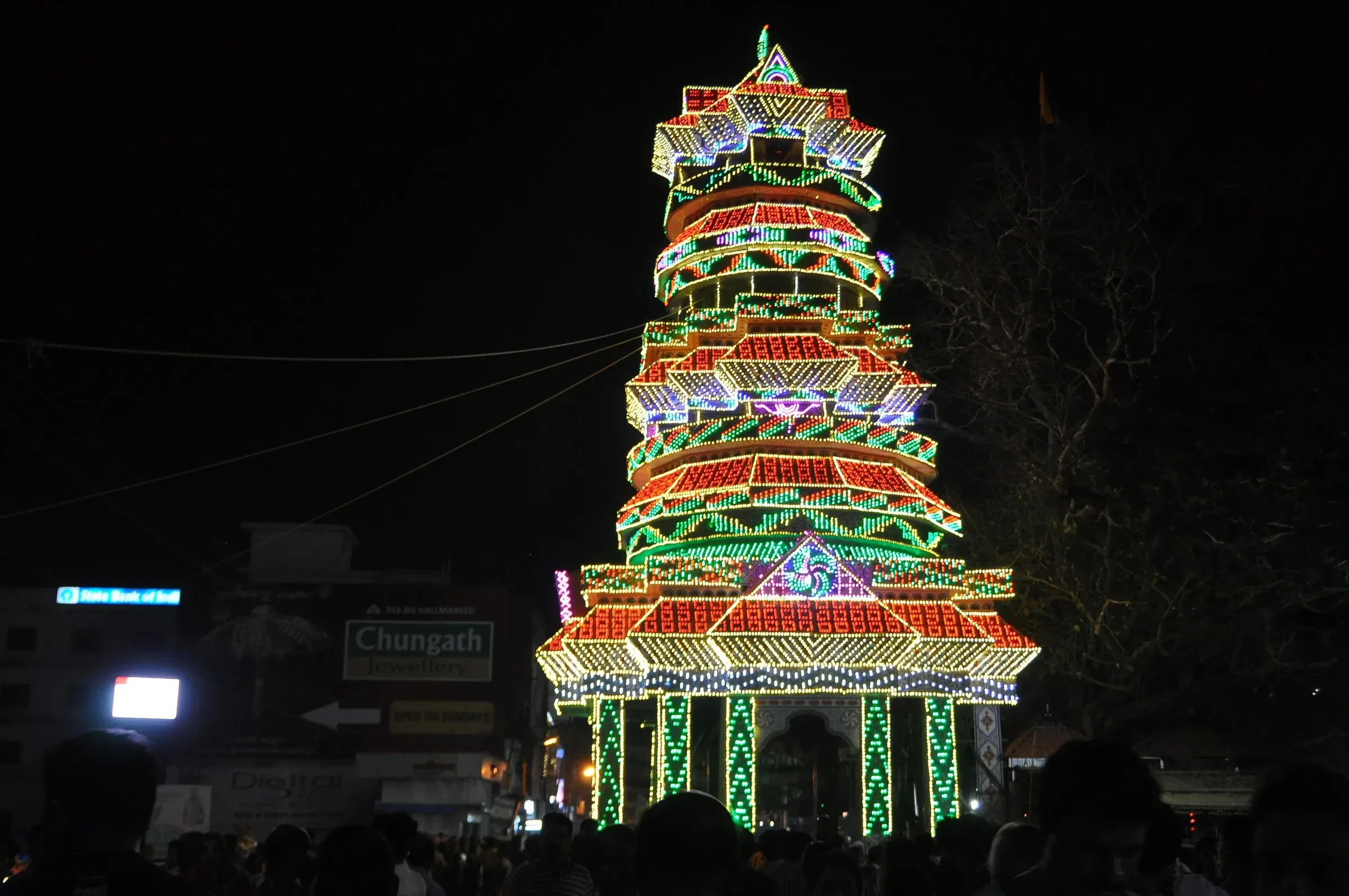 A tall tower of coloured lights lit up at night during a past Thrissur Pooram