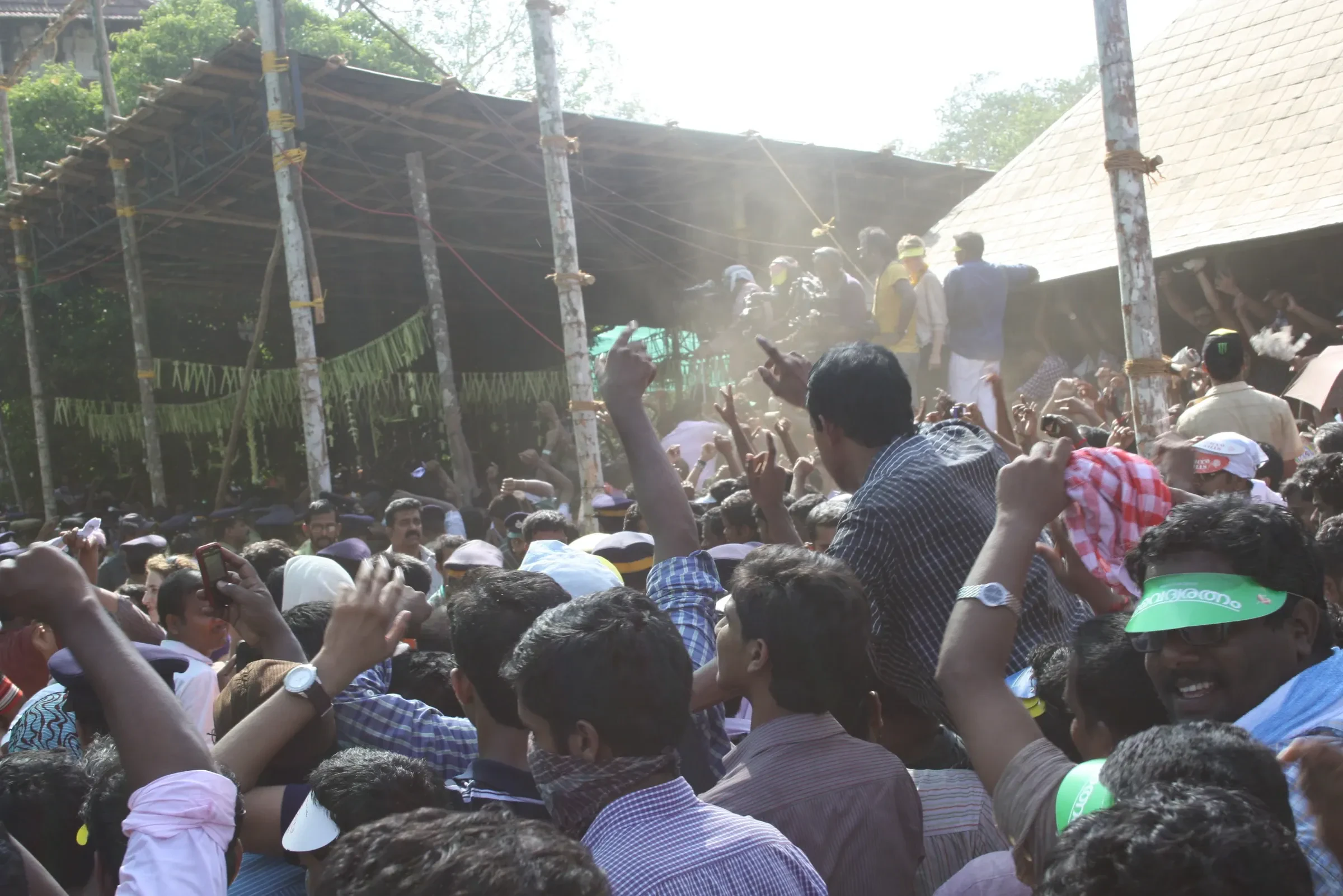 A packed crowd with raised hands beside the temple grounds during a past Thrissur Pooram