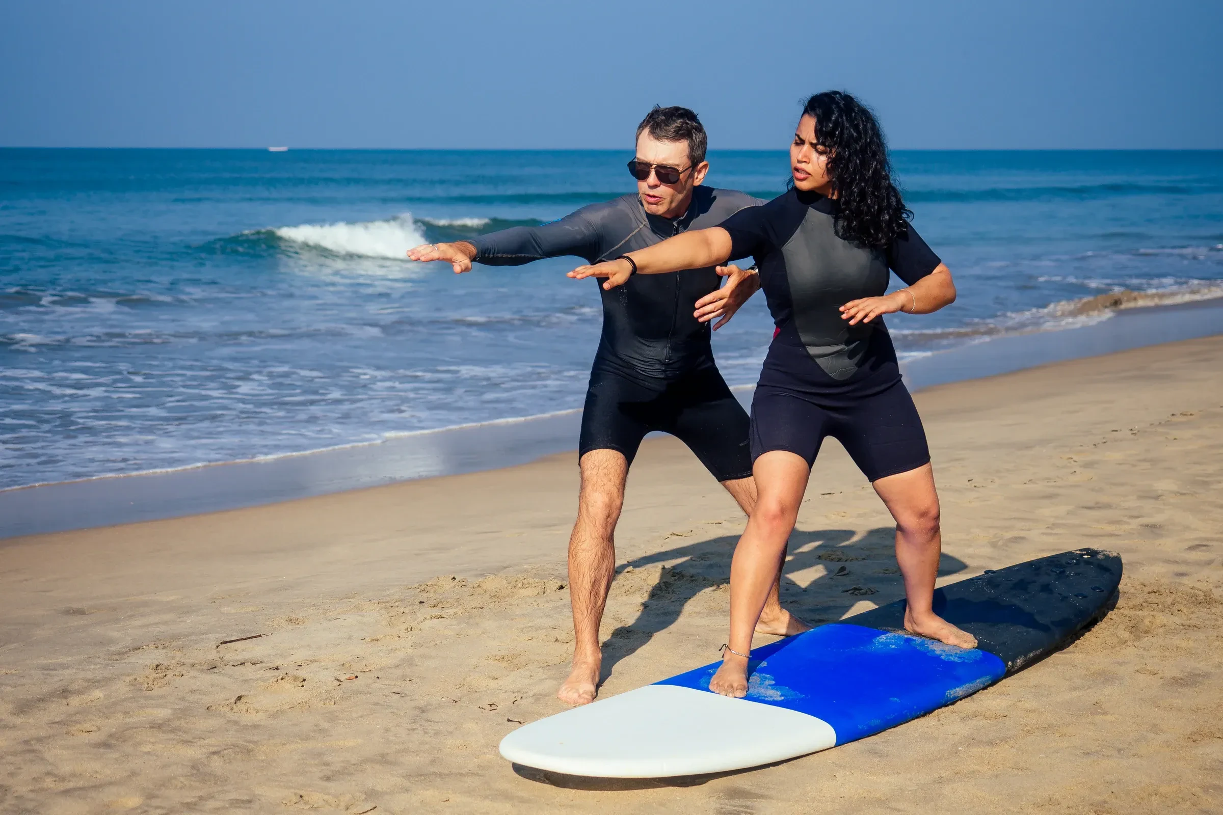 A surf instructor showing a beginner how to stand up on a board on a beach