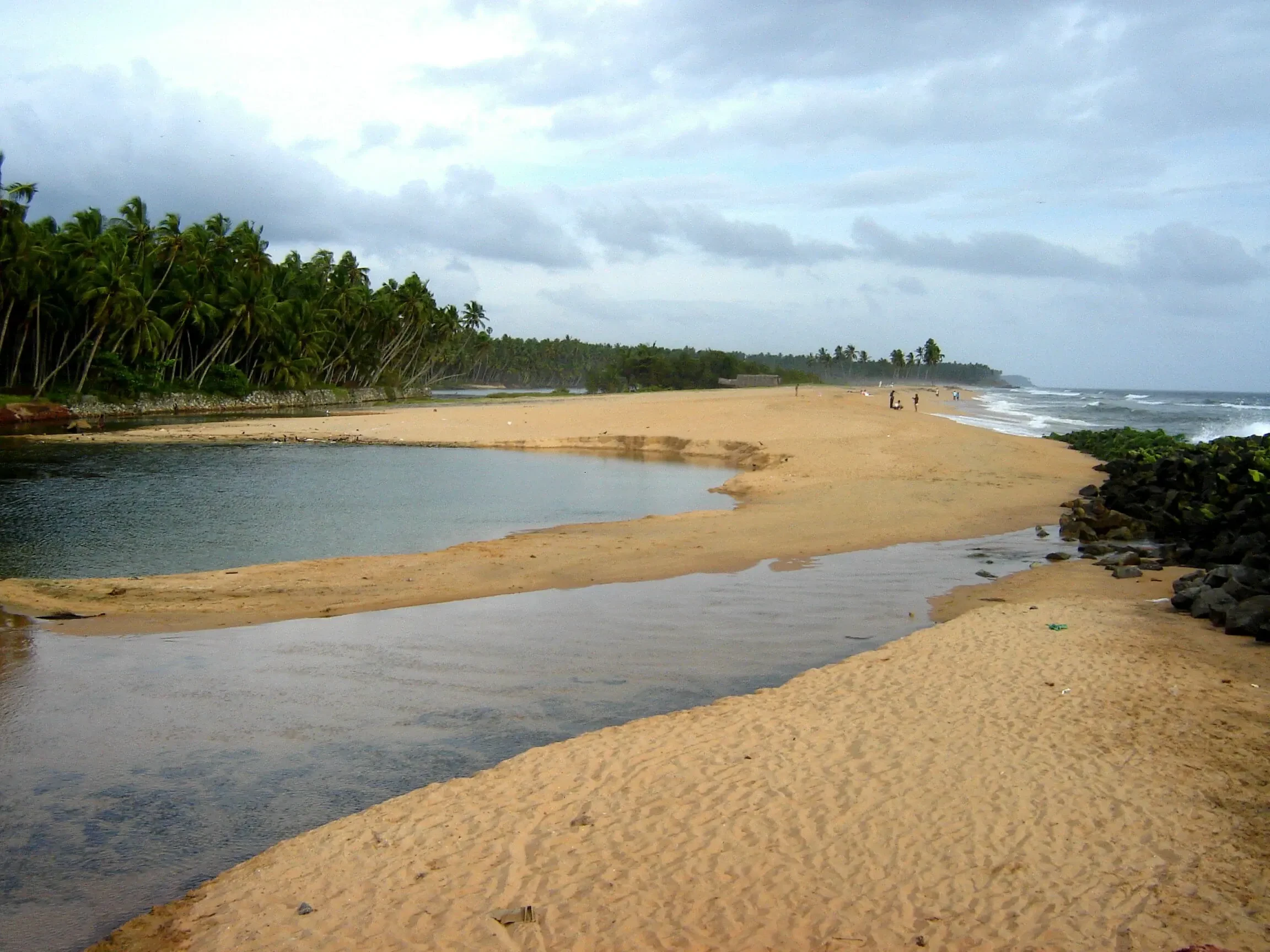 A palm-fringed lagoon channel crossing the sand toward the sea at Kappil