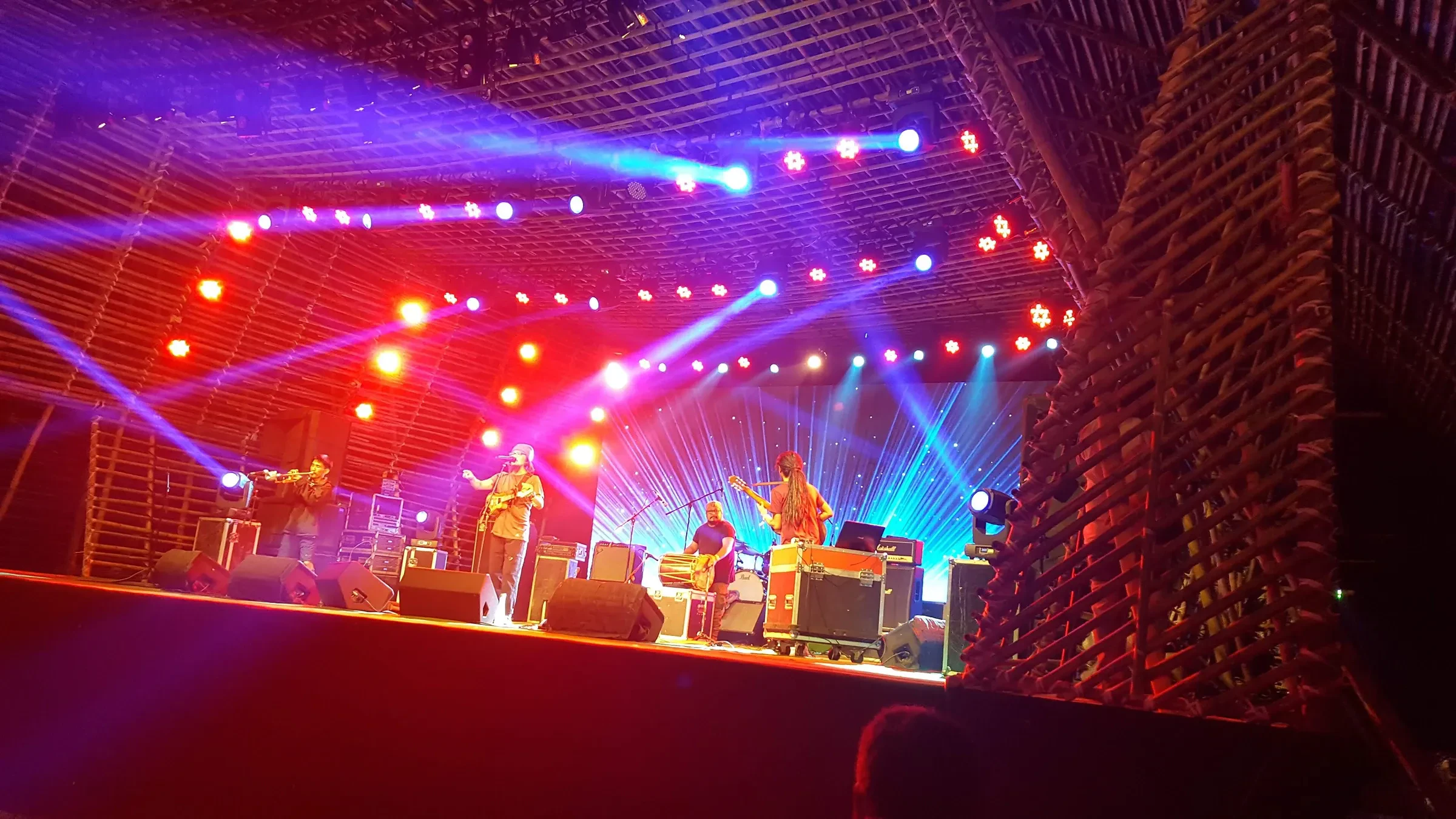Band playing on a bamboo-framed stage under red and blue lights at the Ziro Festival of Music, 2019 edition