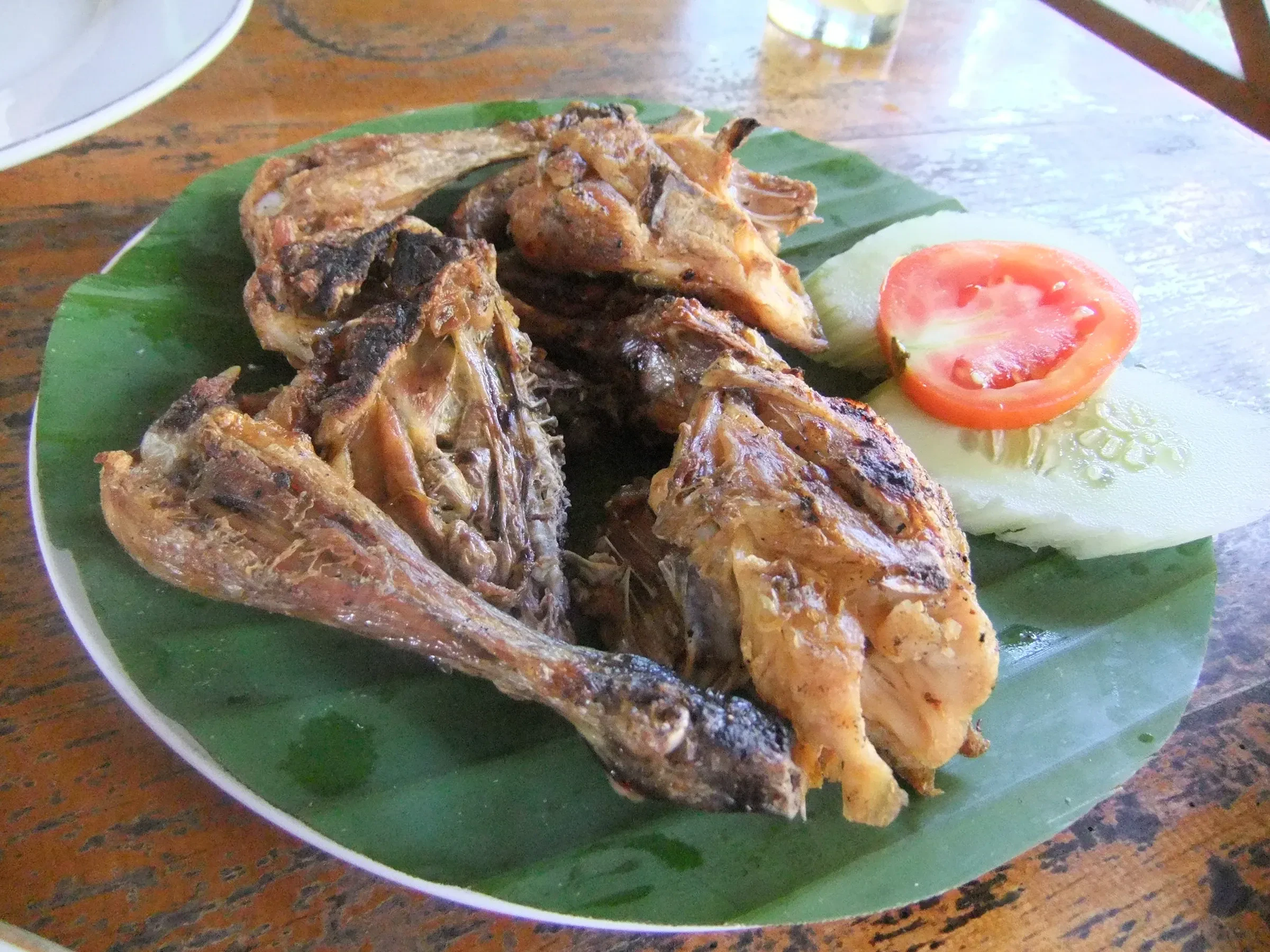 Grilled ayam taliwang chicken on a banana leaf with cucumber and tomato