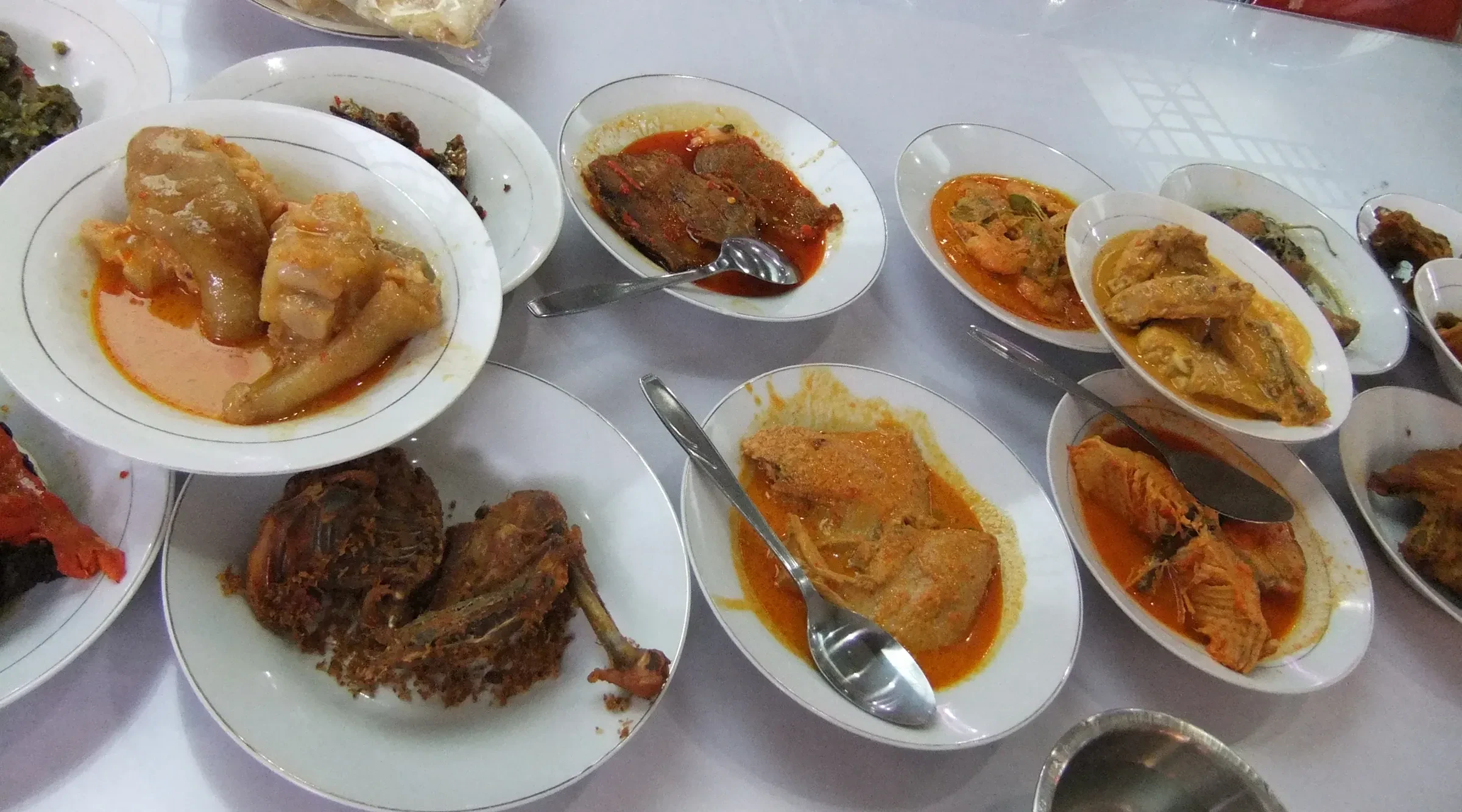 Plates of Padang cuisine laid out on a table, with curries and fried dishes