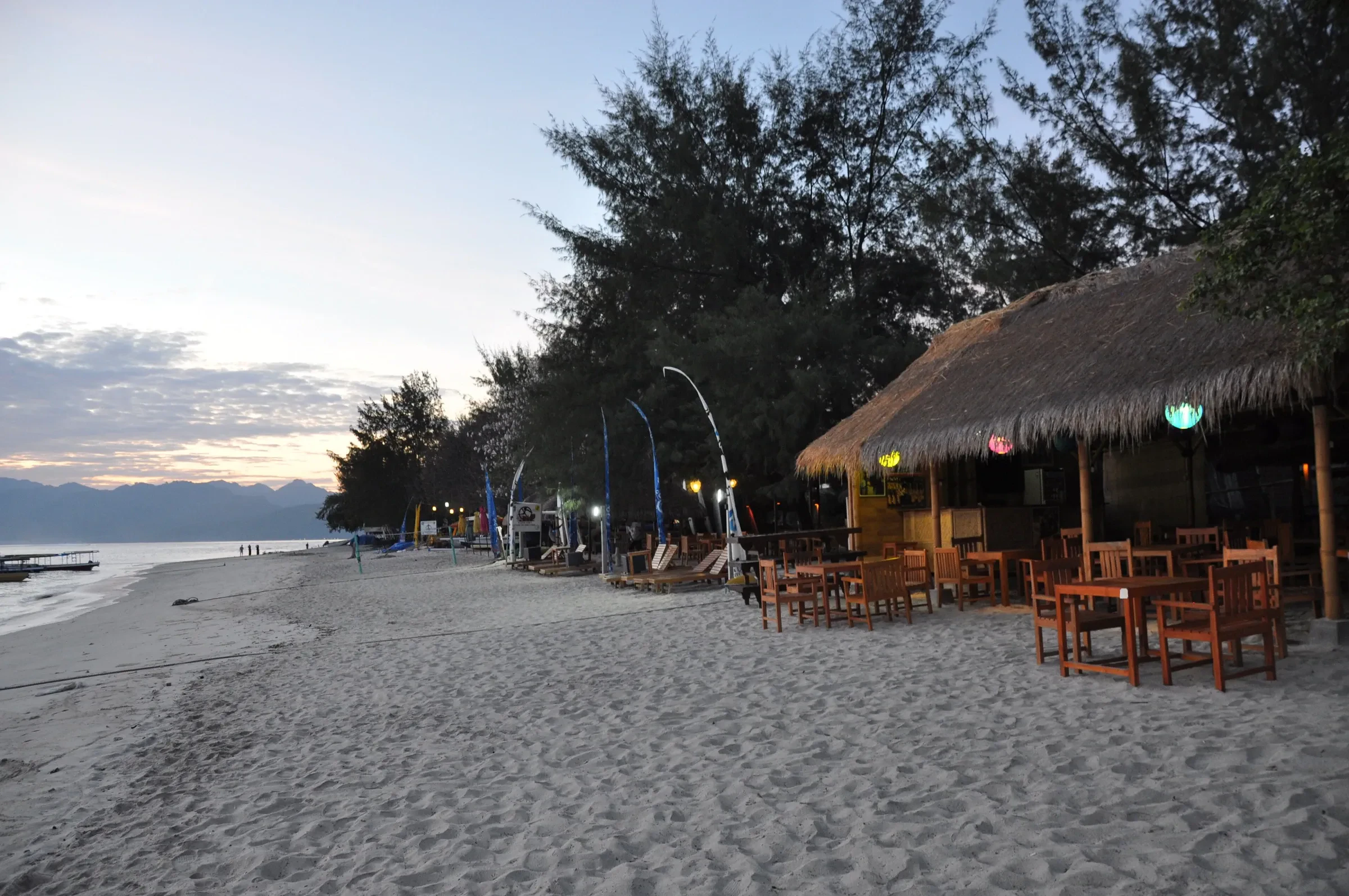 A thatched beach bar with tables on the sand at Gili Trawangan in the evening light