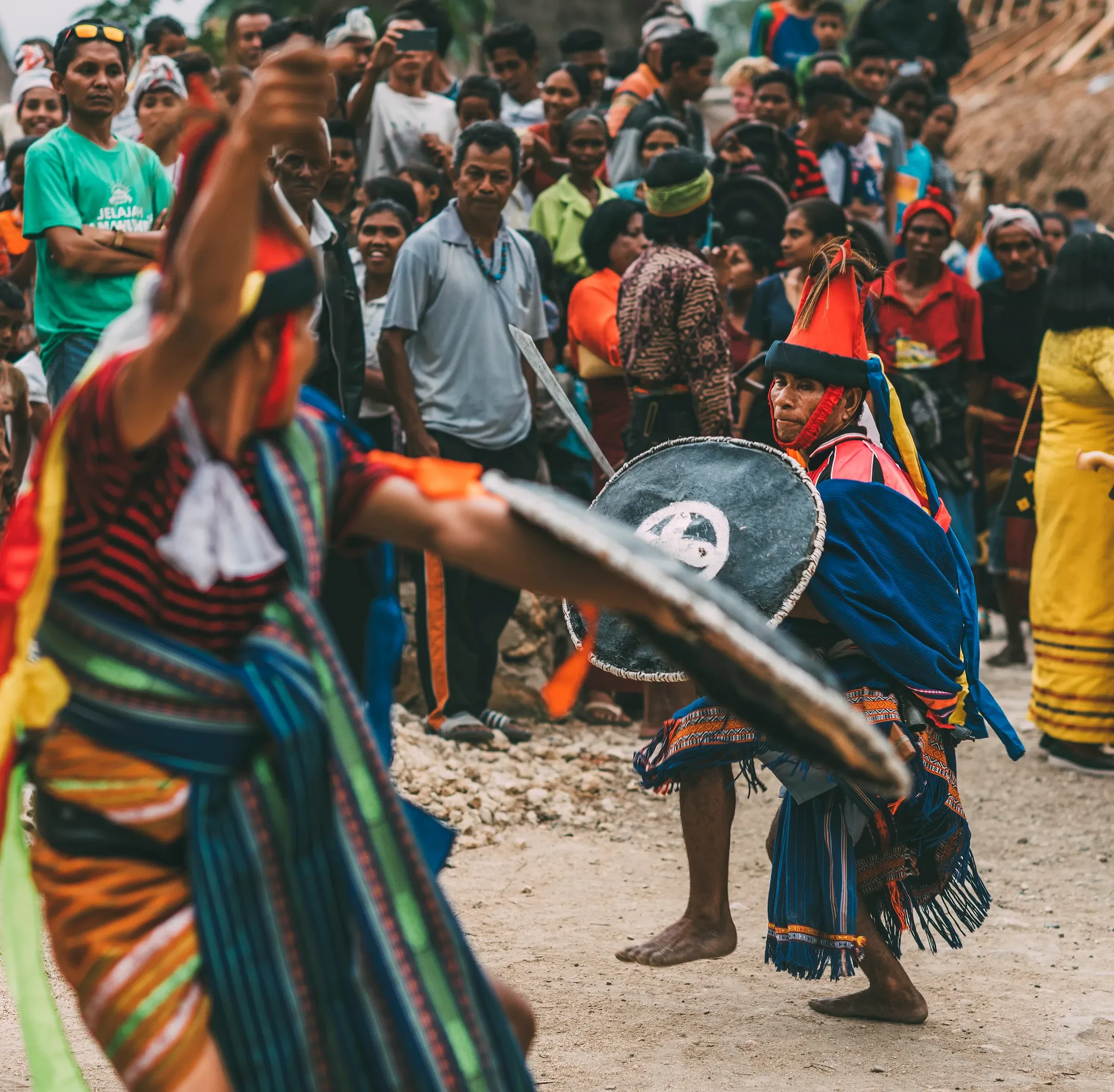 Men in Sumbanese dress perform the Kataga war dance with swords and shields in front of a crowd in West Sumba