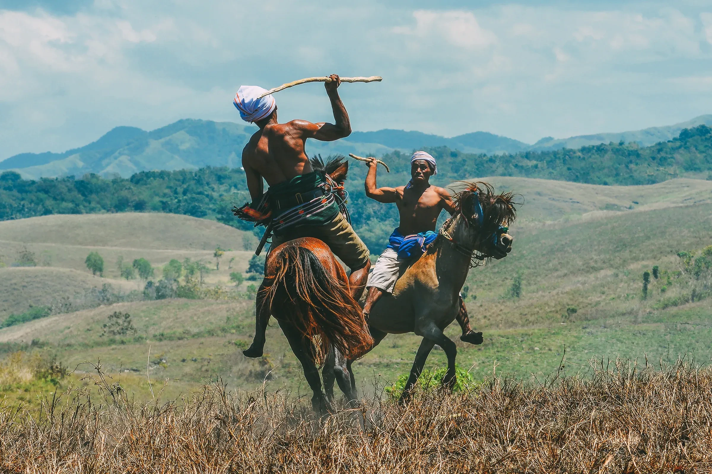 Two riders on horseback with raised wooden spears at a Pasola ceremony on Sumba