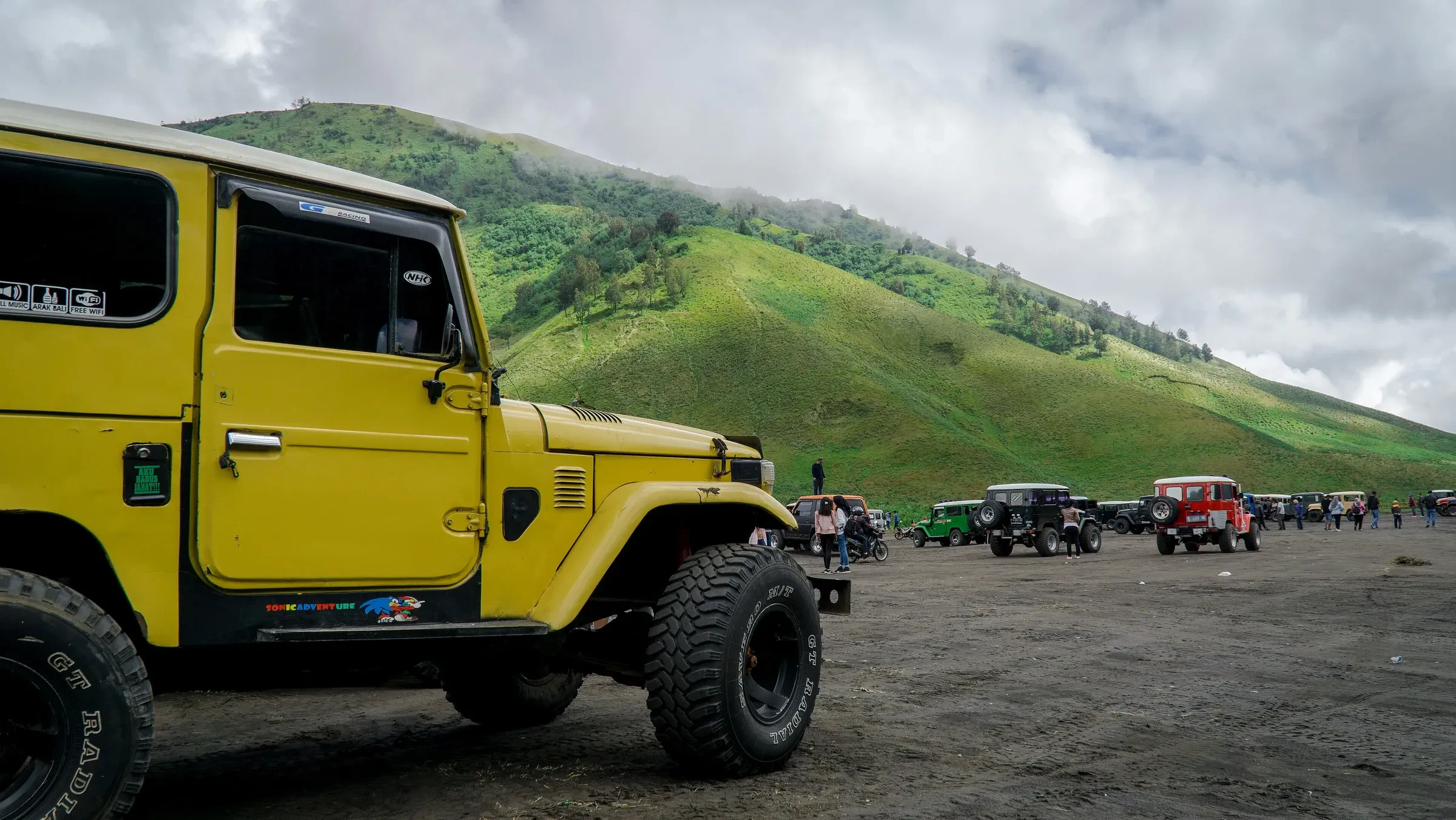 A yellow 4WD jeep in front of a line of jeeps on Bromo's sandy plain