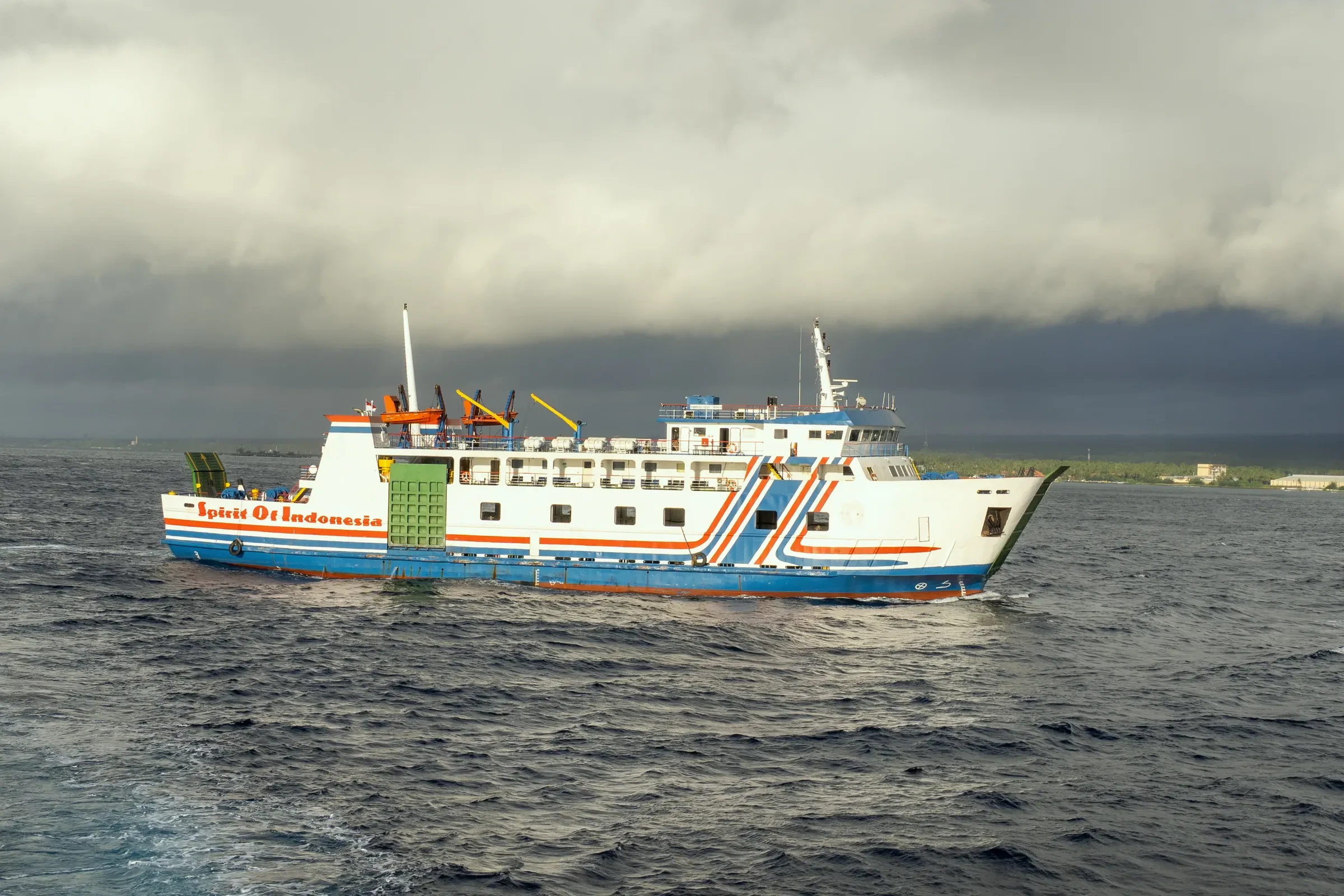 A passenger ferry sailing across the Bali Strait under storm clouds