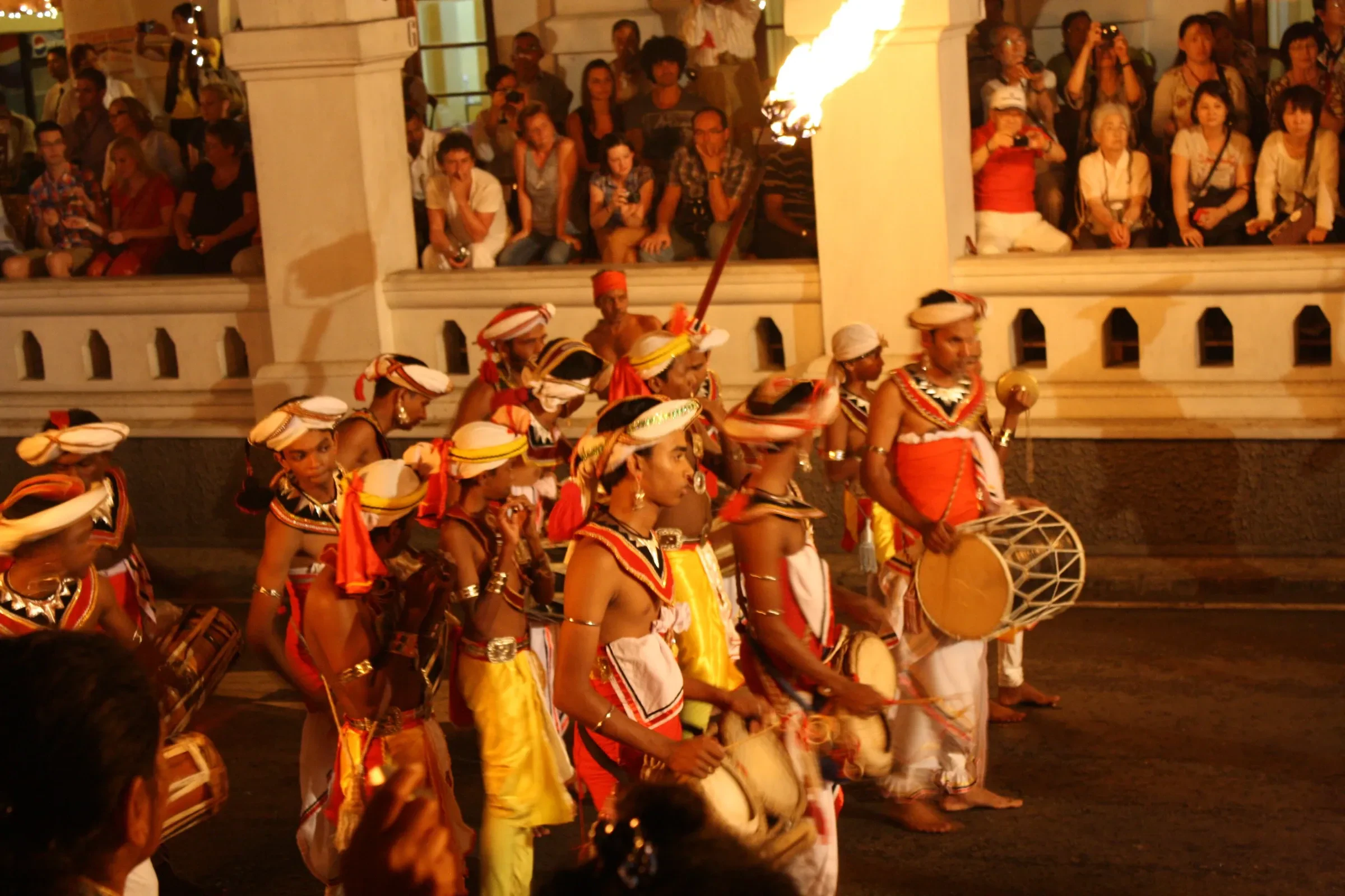 Drummers and a torchbearer passing a crowded balcony during the Esala Perahera in Kandy