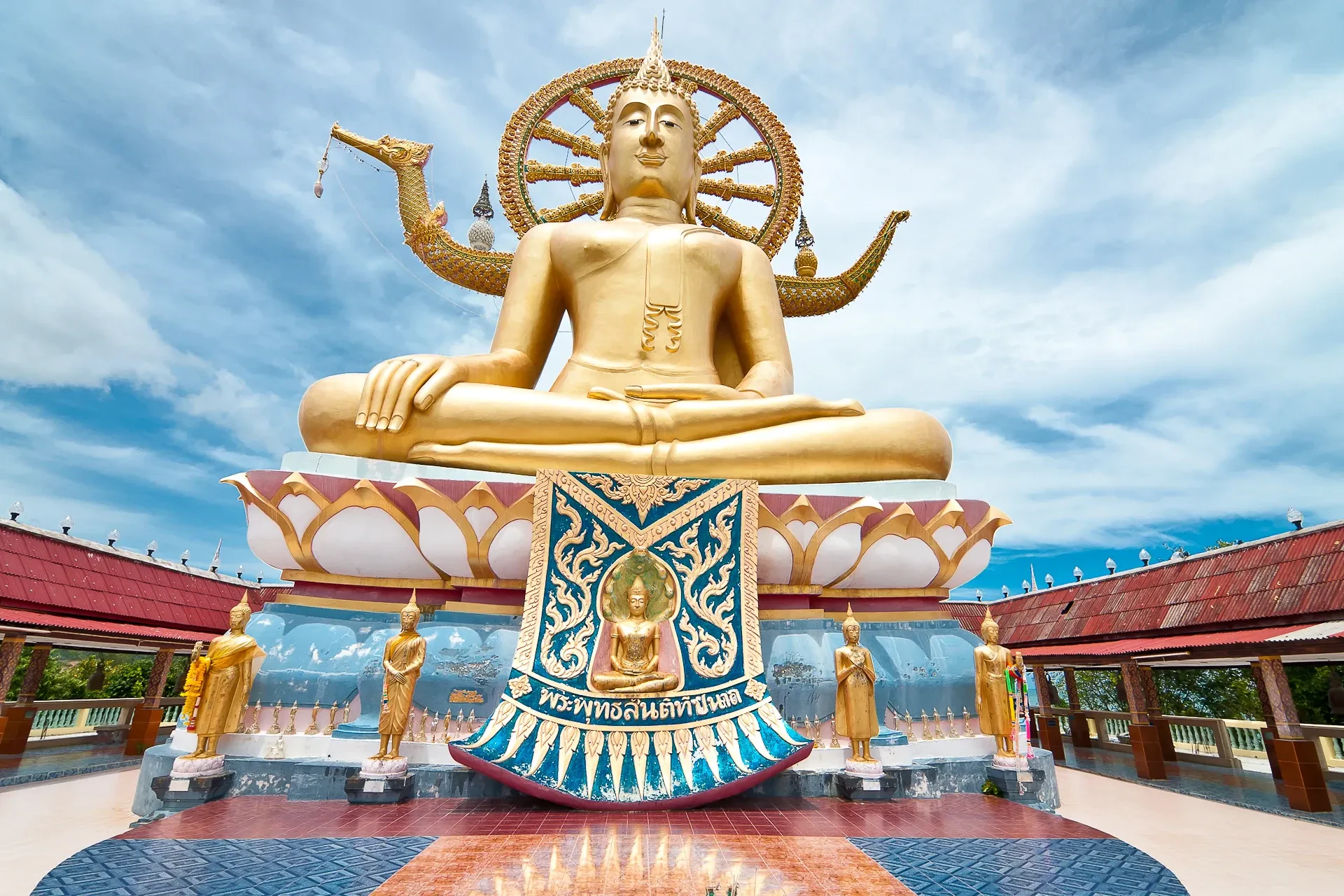 The golden seated Big Buddha statue at Wat Phra Yai on Koh Samui, seen from below against a cloudy sky