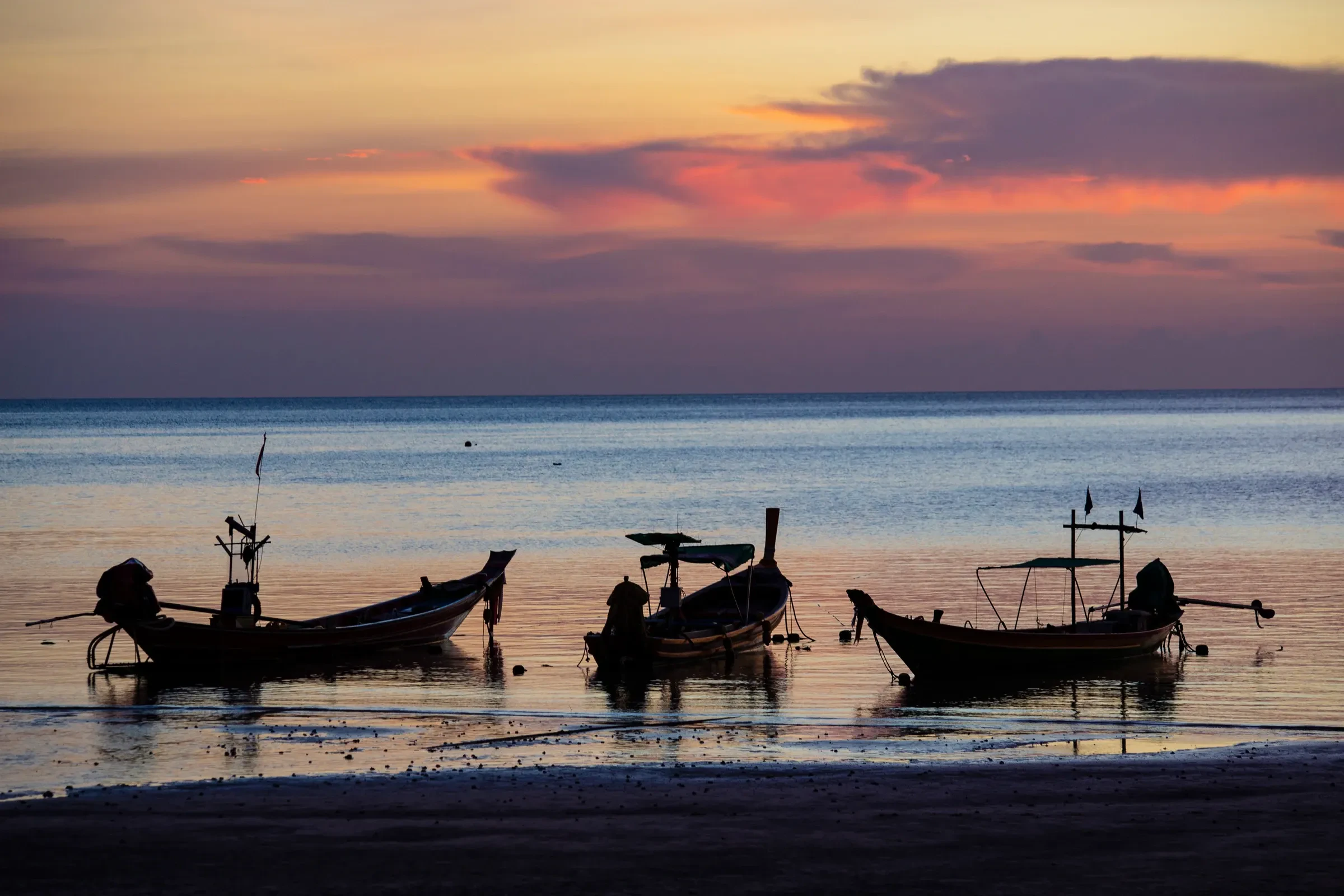 Longtail boats silhouetted against an orange sunset sky on Sairee Beach, Koh Tao