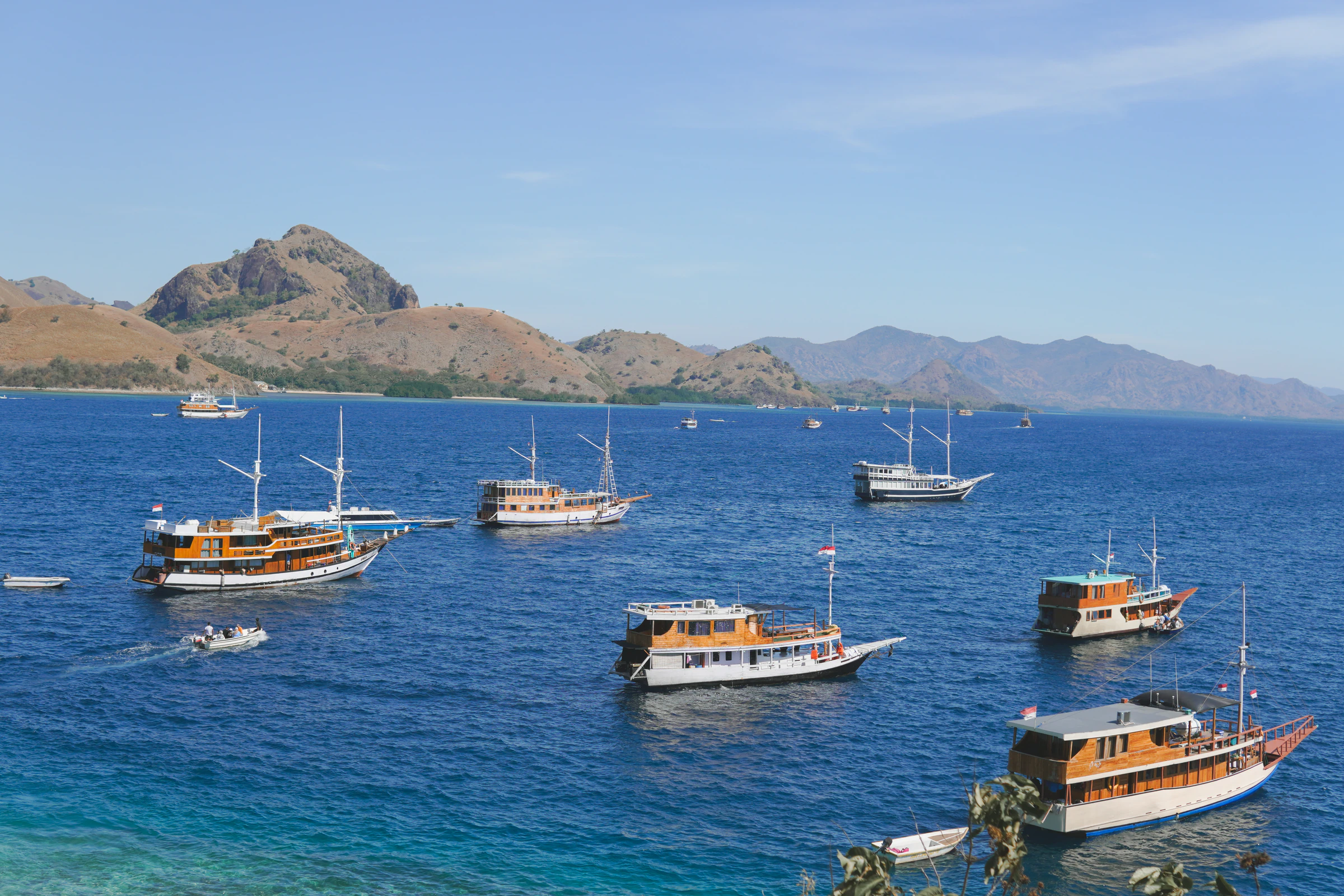 Wooden phinisi boats at anchor off Labuan Bajo, with the dry hills of the park behind