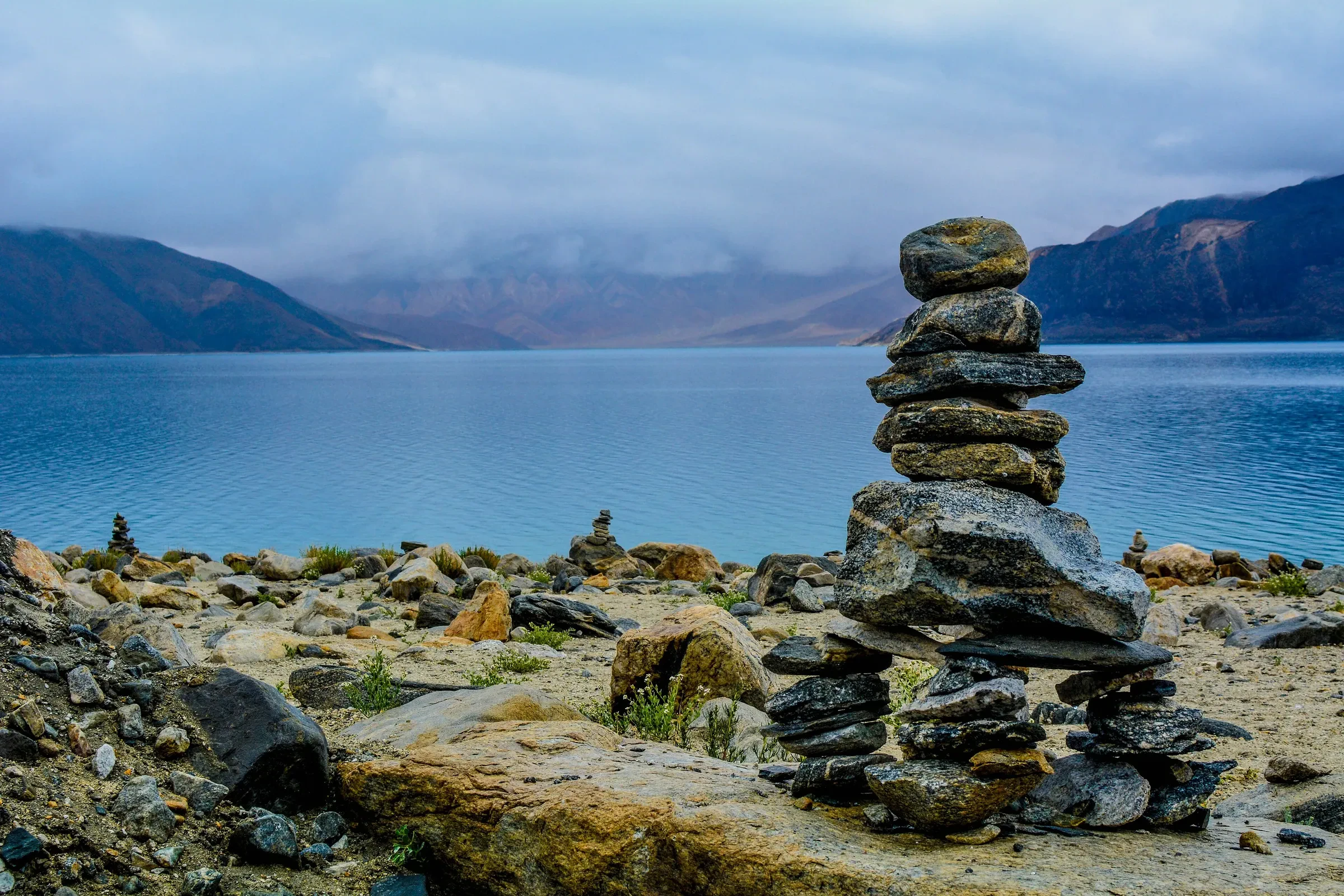 Stacked stones on the shore of Pangong Tso with mountains across the lake
