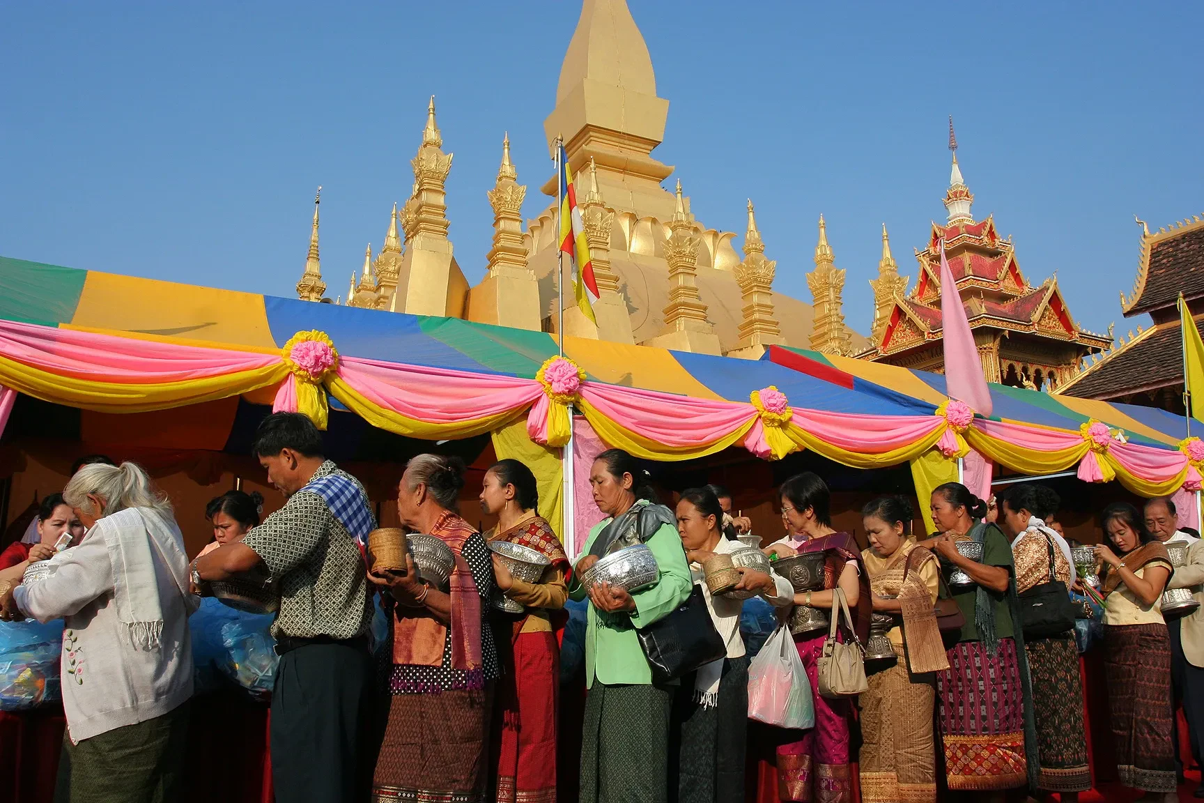 Festival-goers queueing beside coloured awnings in front of the golden stupa of Pha That Luang