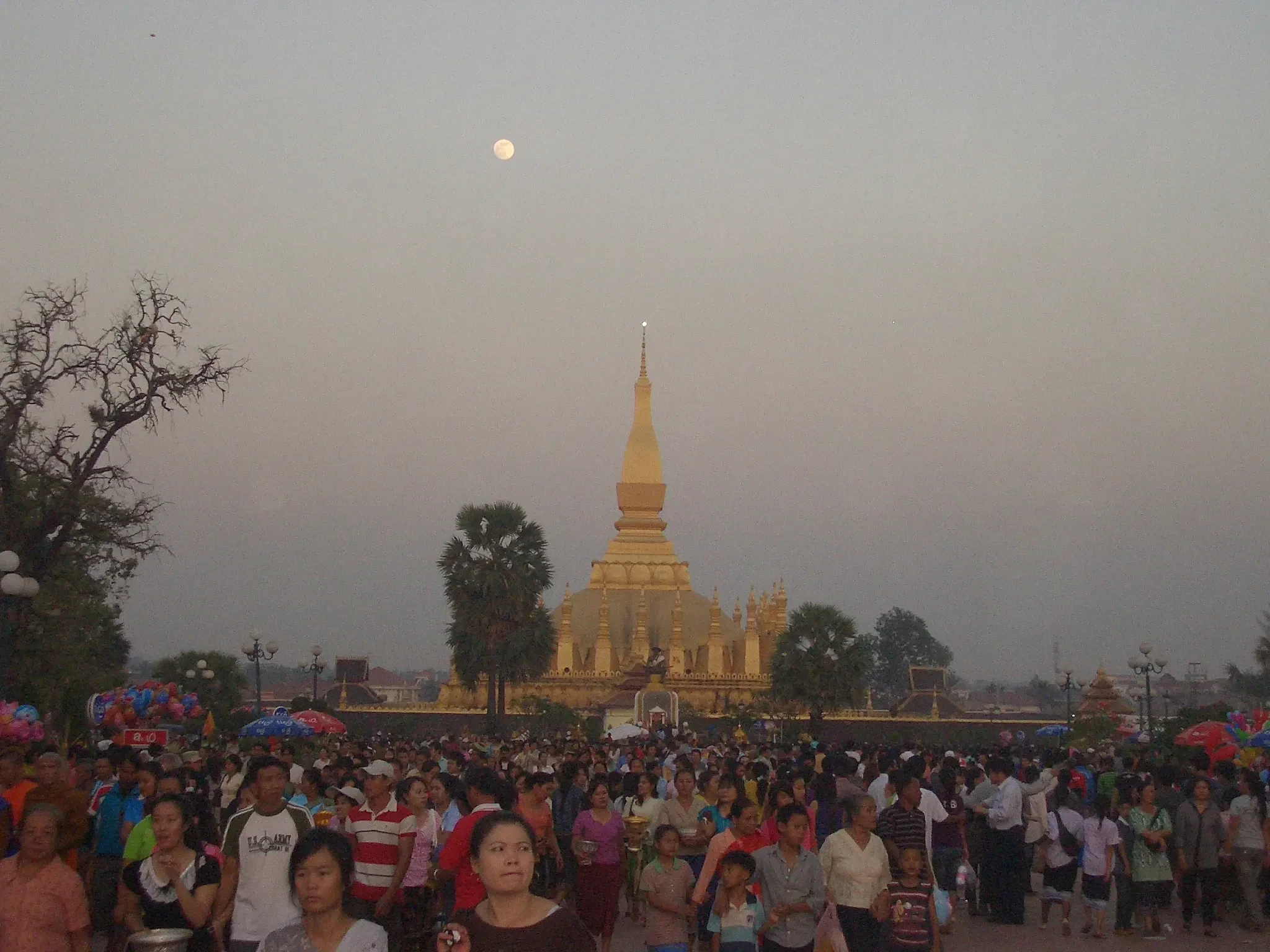 The full moon over Pha That Luang as the evening crowd gathers on the esplanade