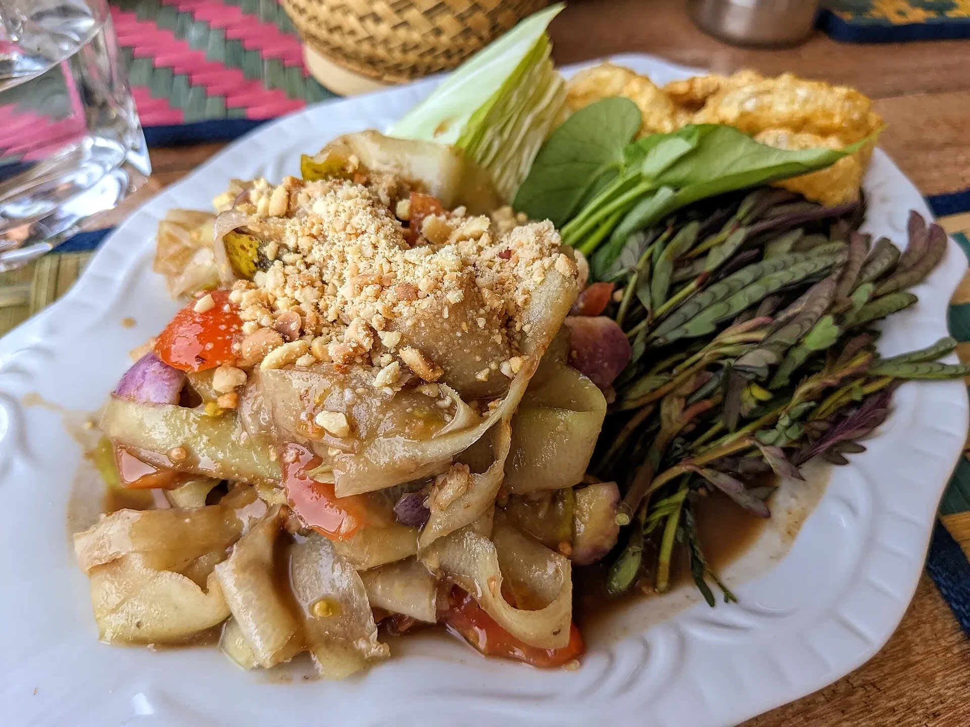 A plate of tam mak hoong, Lao green papaya salad topped with peanuts, with raw vegetables on the side