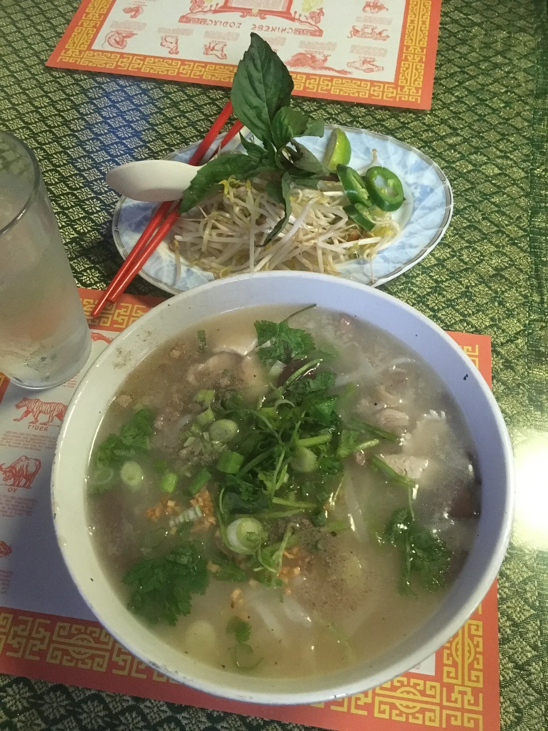 A bowl of khao piak sen, a thick rice noodle soup, next to a plate of fresh herbs