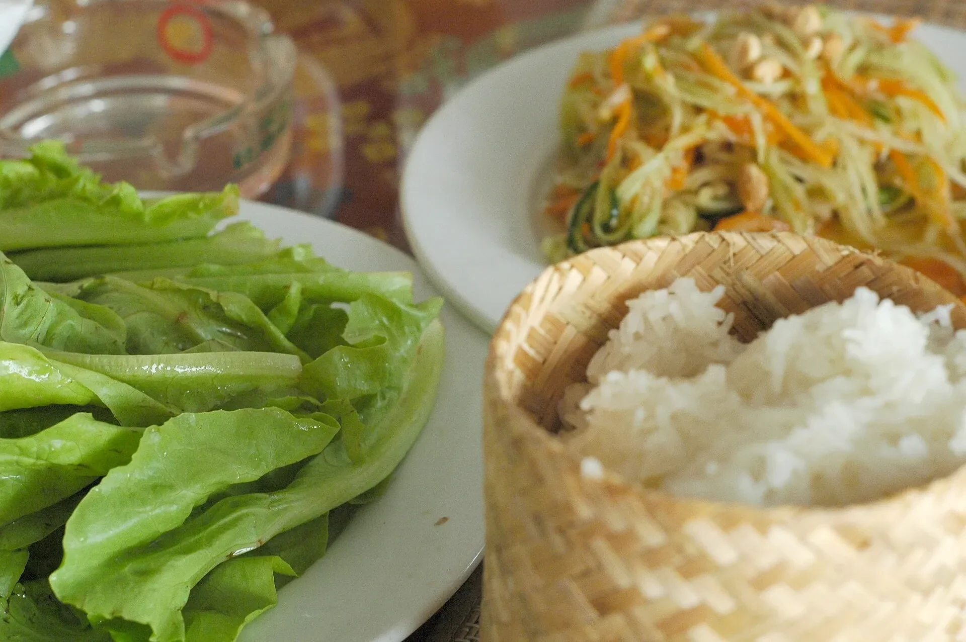 Sticky rice in a small woven basket beside lettuce and papaya salad