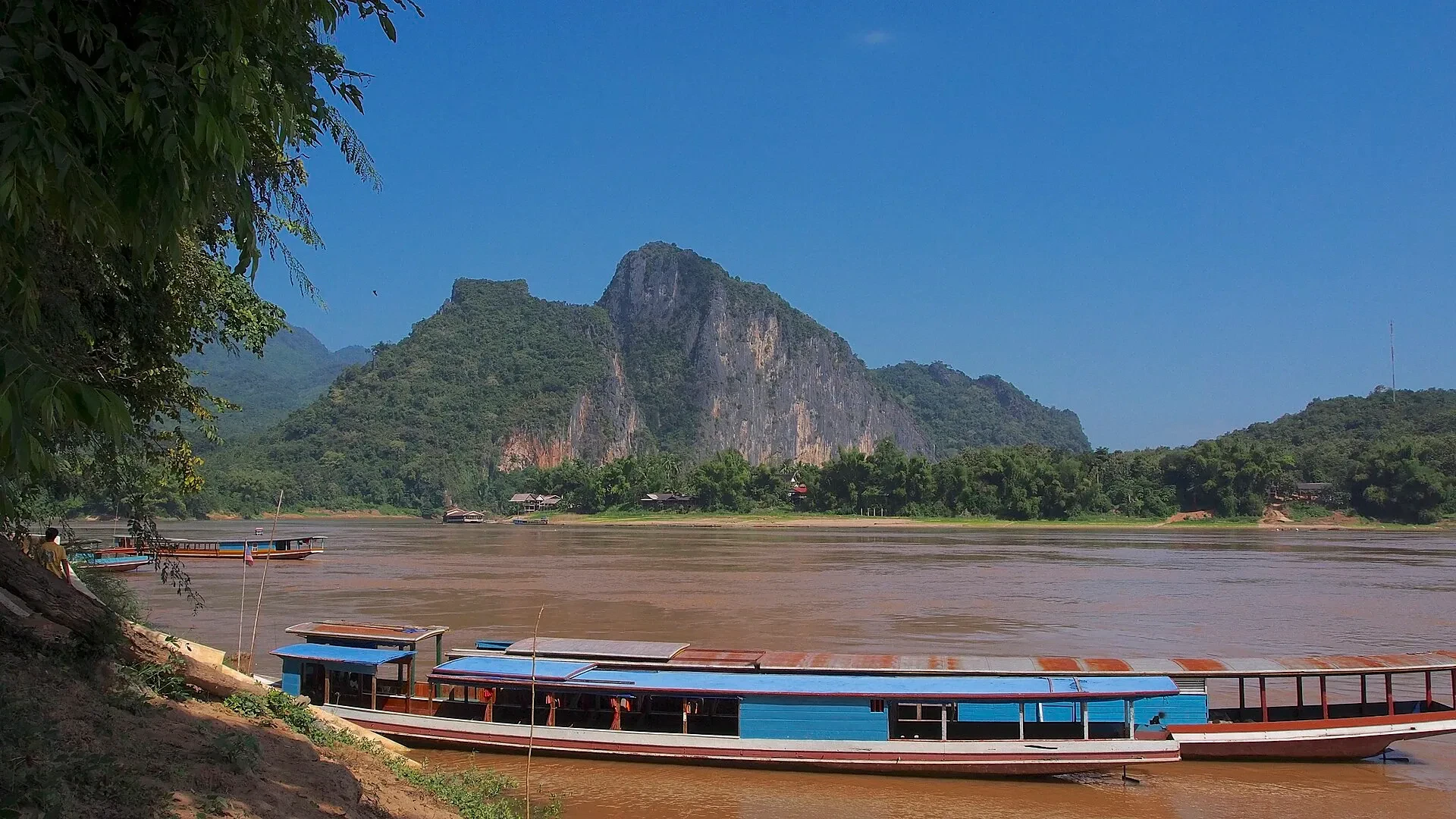 A long boat on the Mekong at the Pak Ou caves landing, with a rocky hill behind
