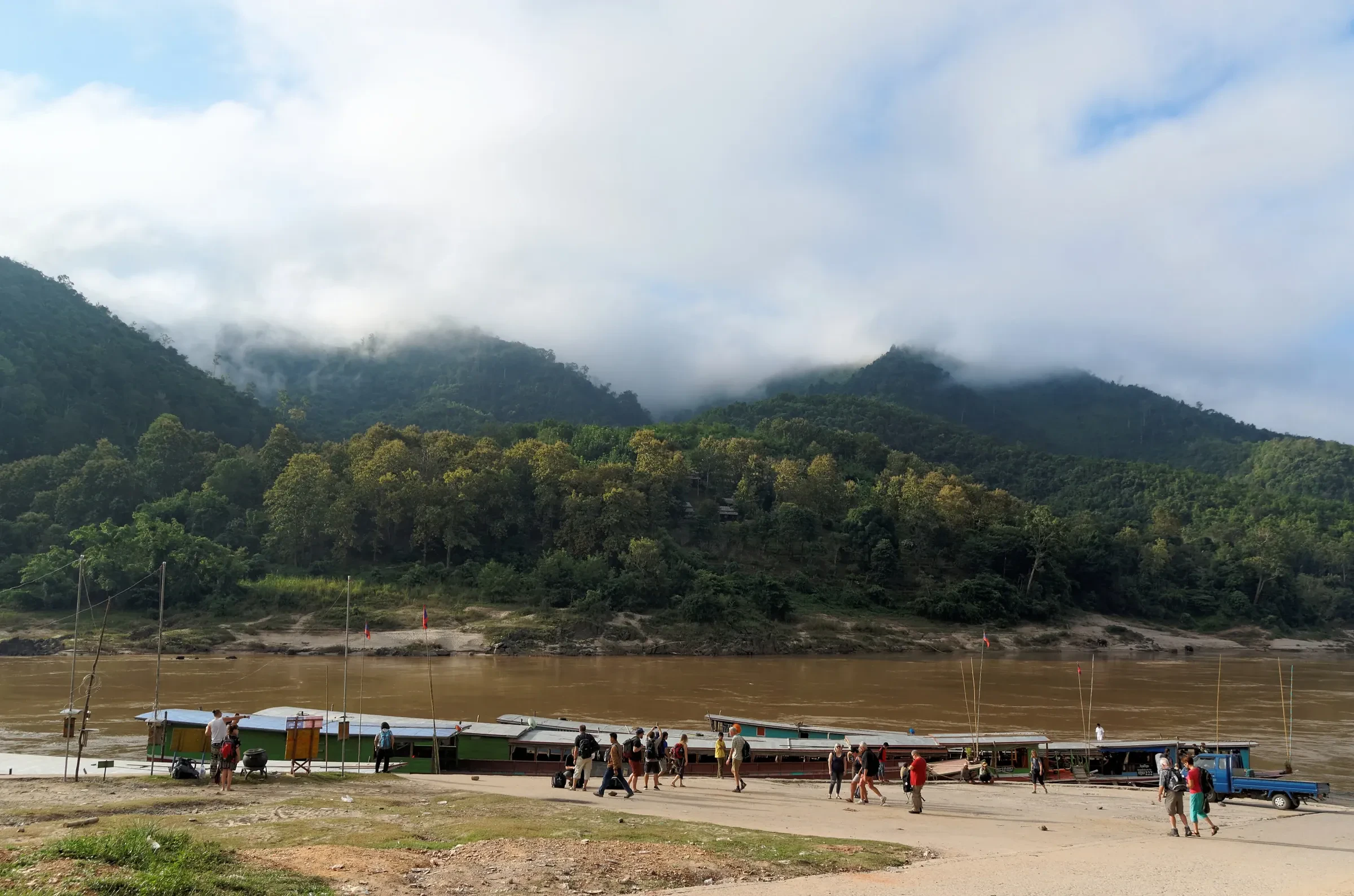 Slow boats pulled up on the Mekong shore at Pak Beng, with low cloud over the hills behind