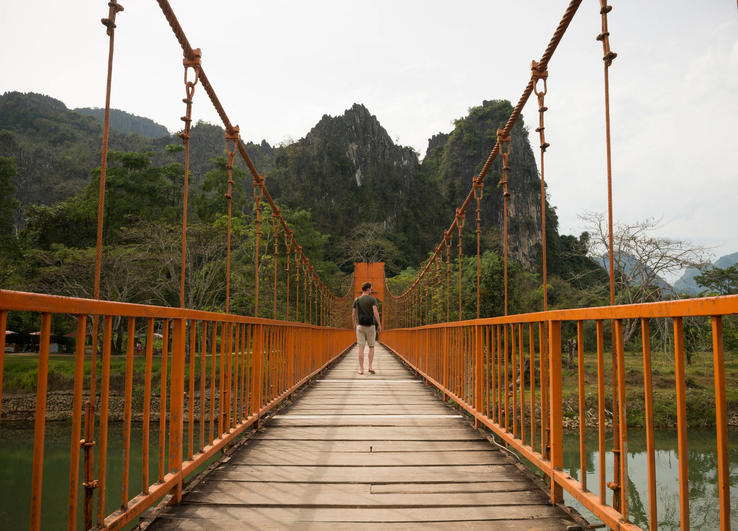 A traveller crossing a river on a wooden bridge in Vang Vieng