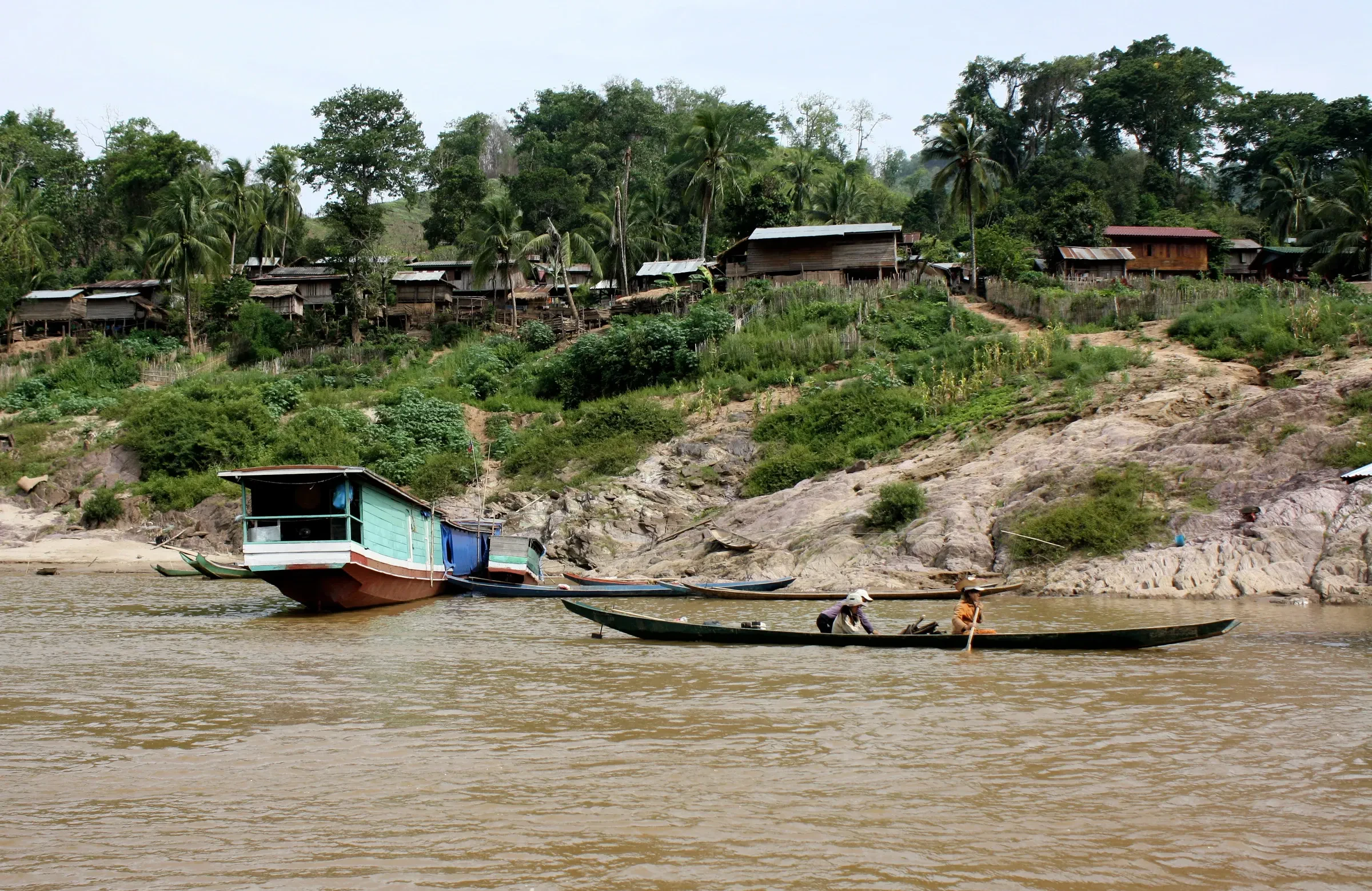 A slow boat and a narrow wooden boat on the Mekong below a riverside village in Laos